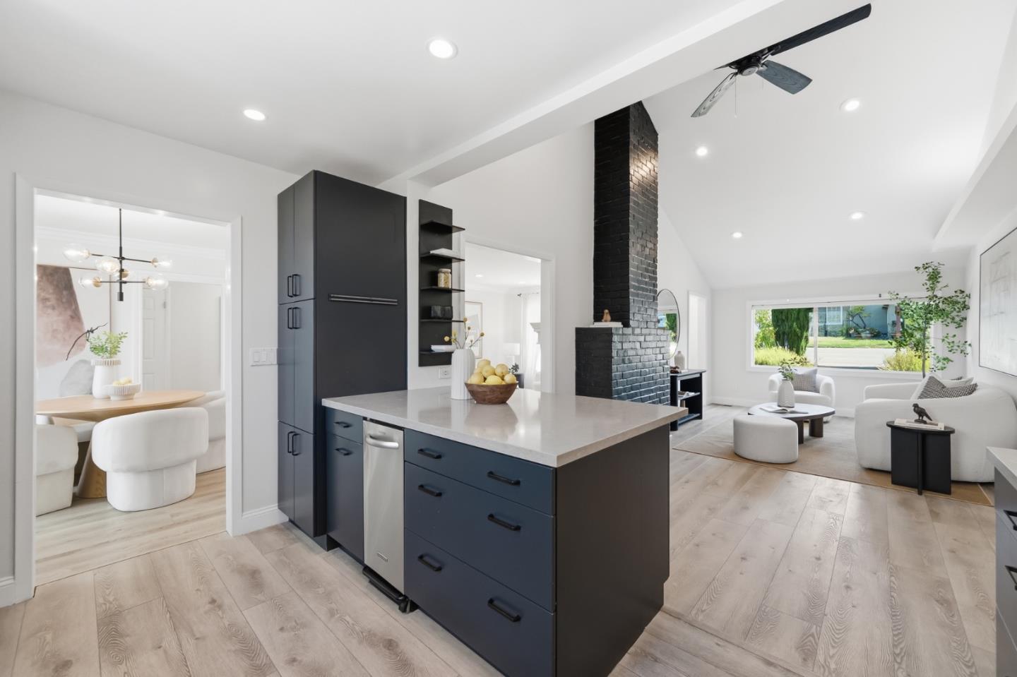 Open-plan kitchen with a dark blue island, black brick fireplace, and bright adjoining living area.