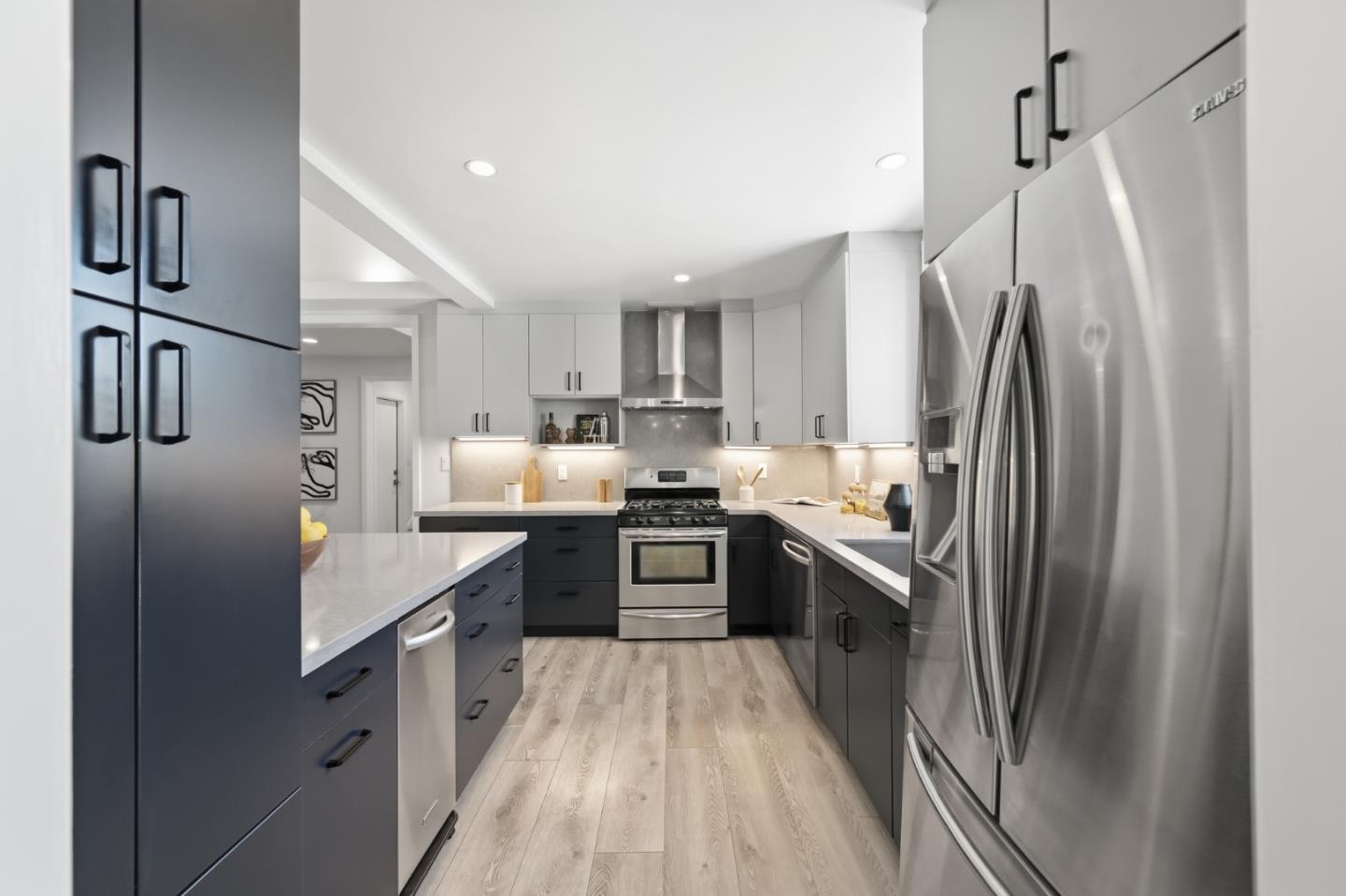 Remodeled kitchen with dark cabinets, white countertops, stainless steel appliances, and light wood floors.