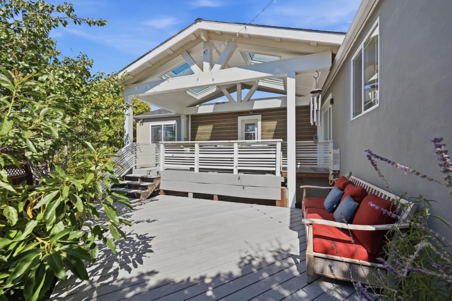 Raised deck with covered patio, white railings, leafy plants, and red-cushioned seating.