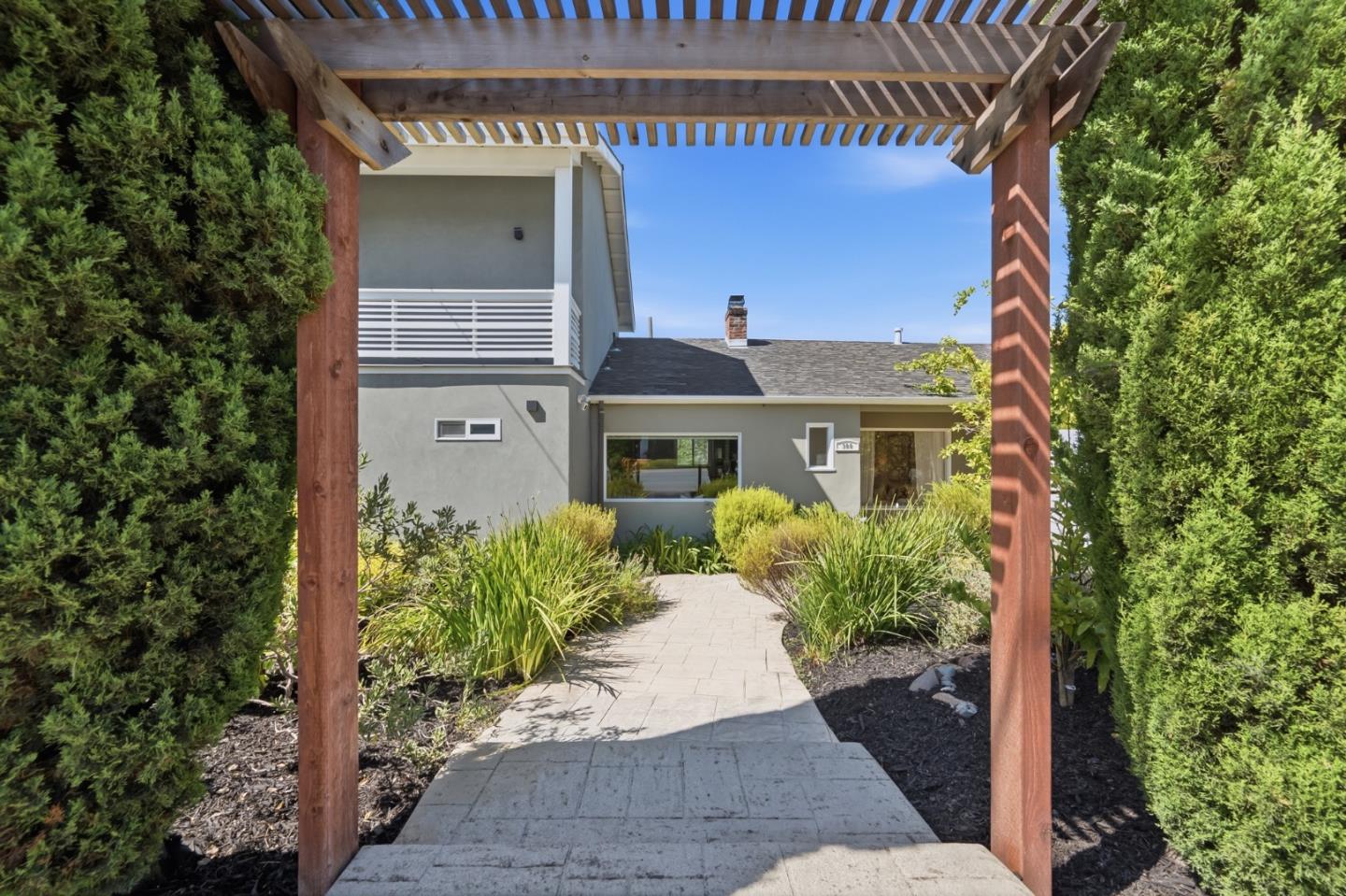 Modern gray home behind a wooden pergola, with a paved walkway and landscaped garden.