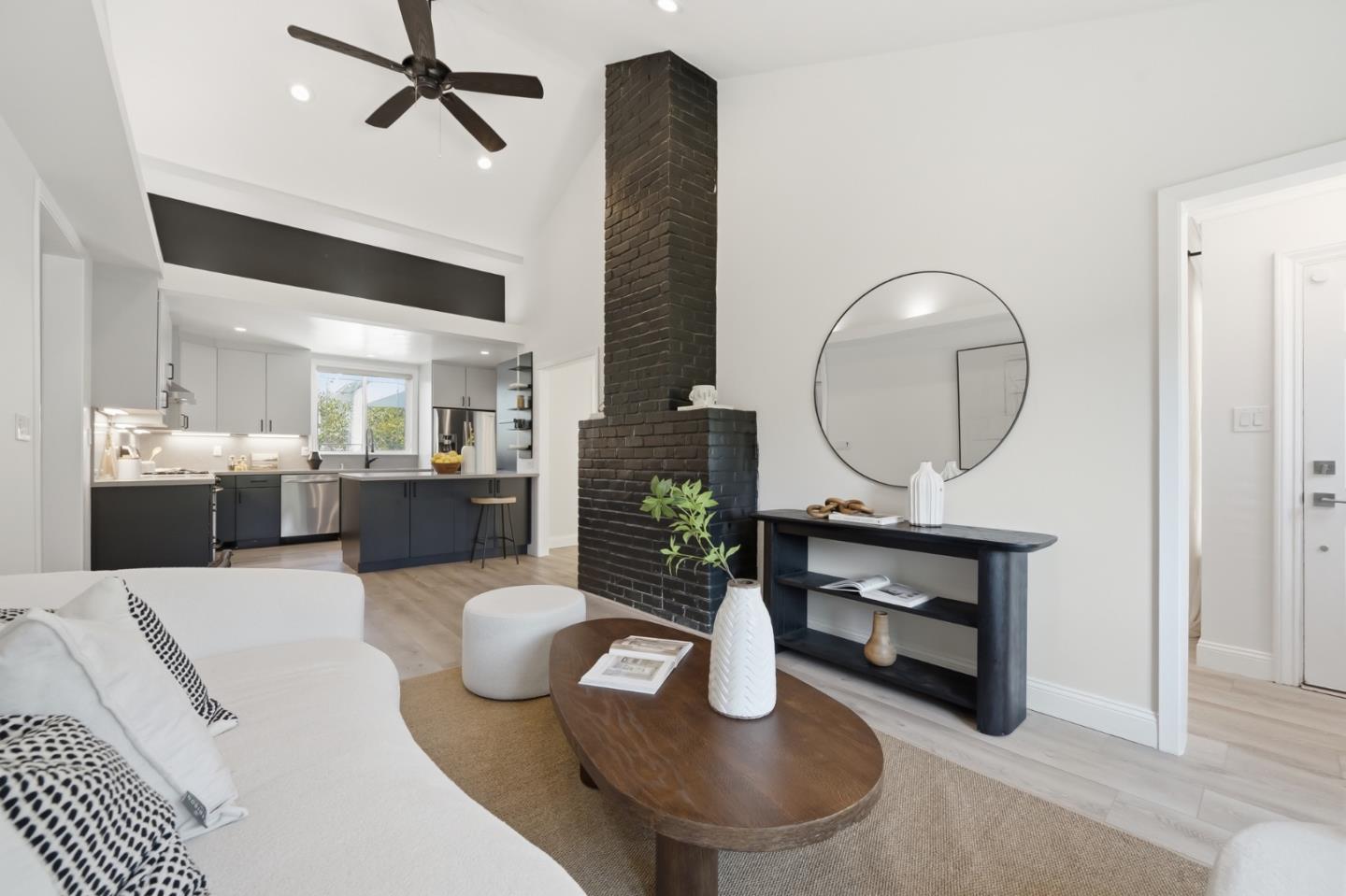 Staged living room with a tall black brick fireplace, white sofa, and open kitchen.