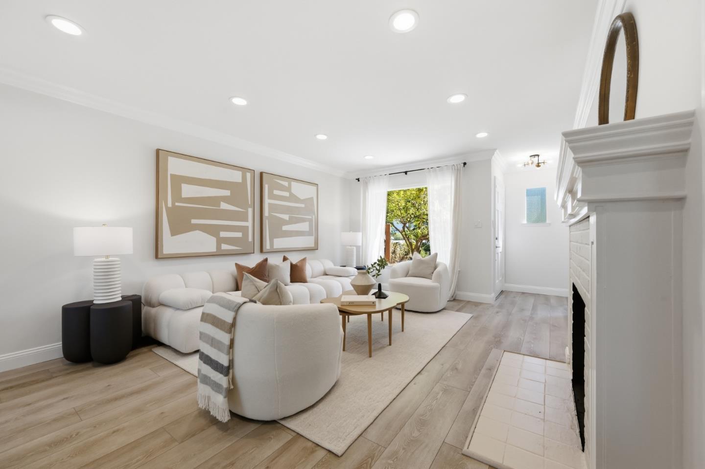 Staged living room with white seating, abstract wall art, light wood floors, and a white fireplace.