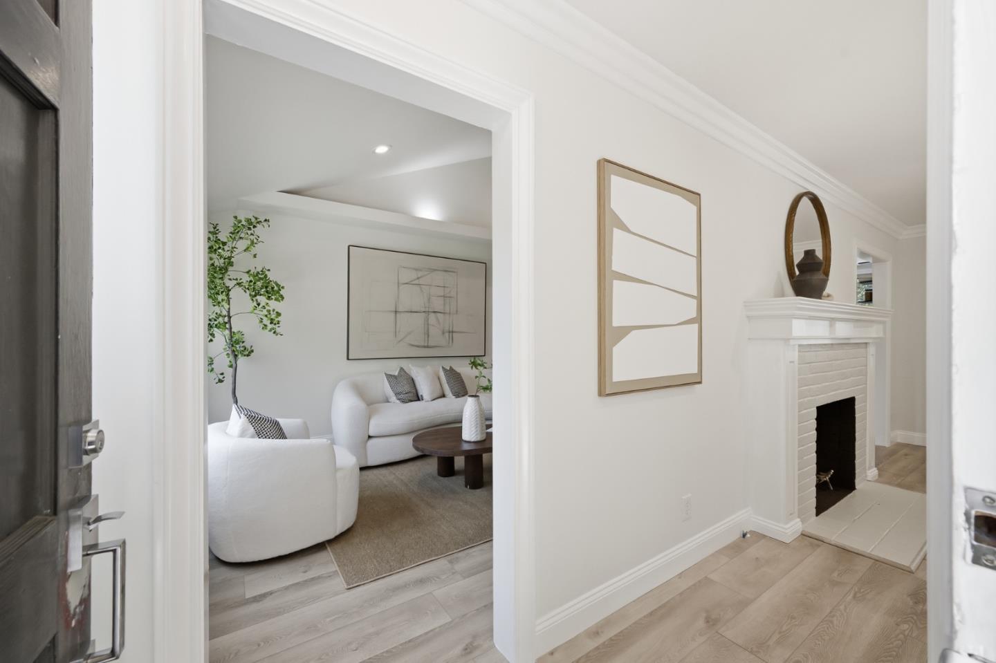 Living room with white sofas and a potted tree, viewed past an entry hall fireplace.