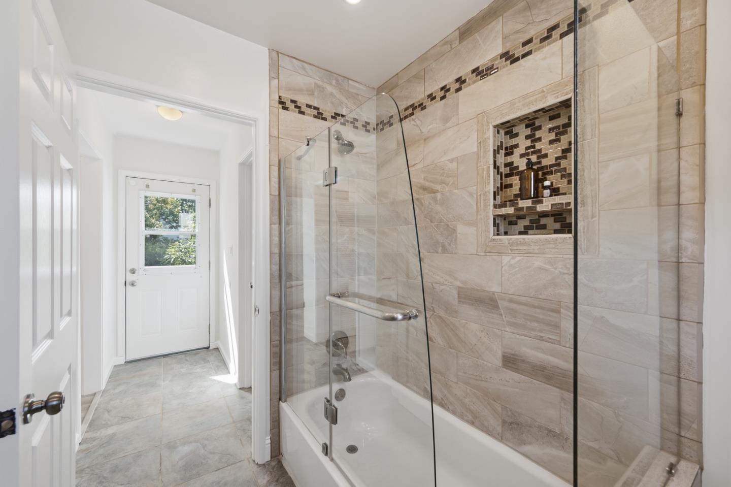 Bathroom with a glass-enclosed tub, beige stone tile, and a recessed shower niche.
