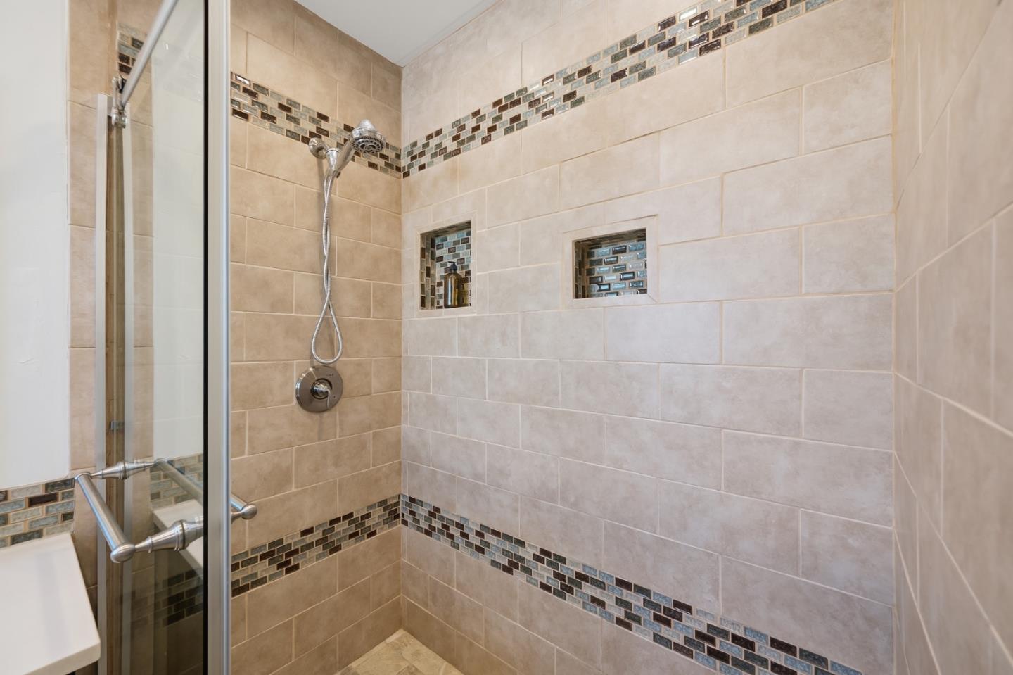 Walk-in shower with beige tile, mosaic accent bands, and two recessed niches.