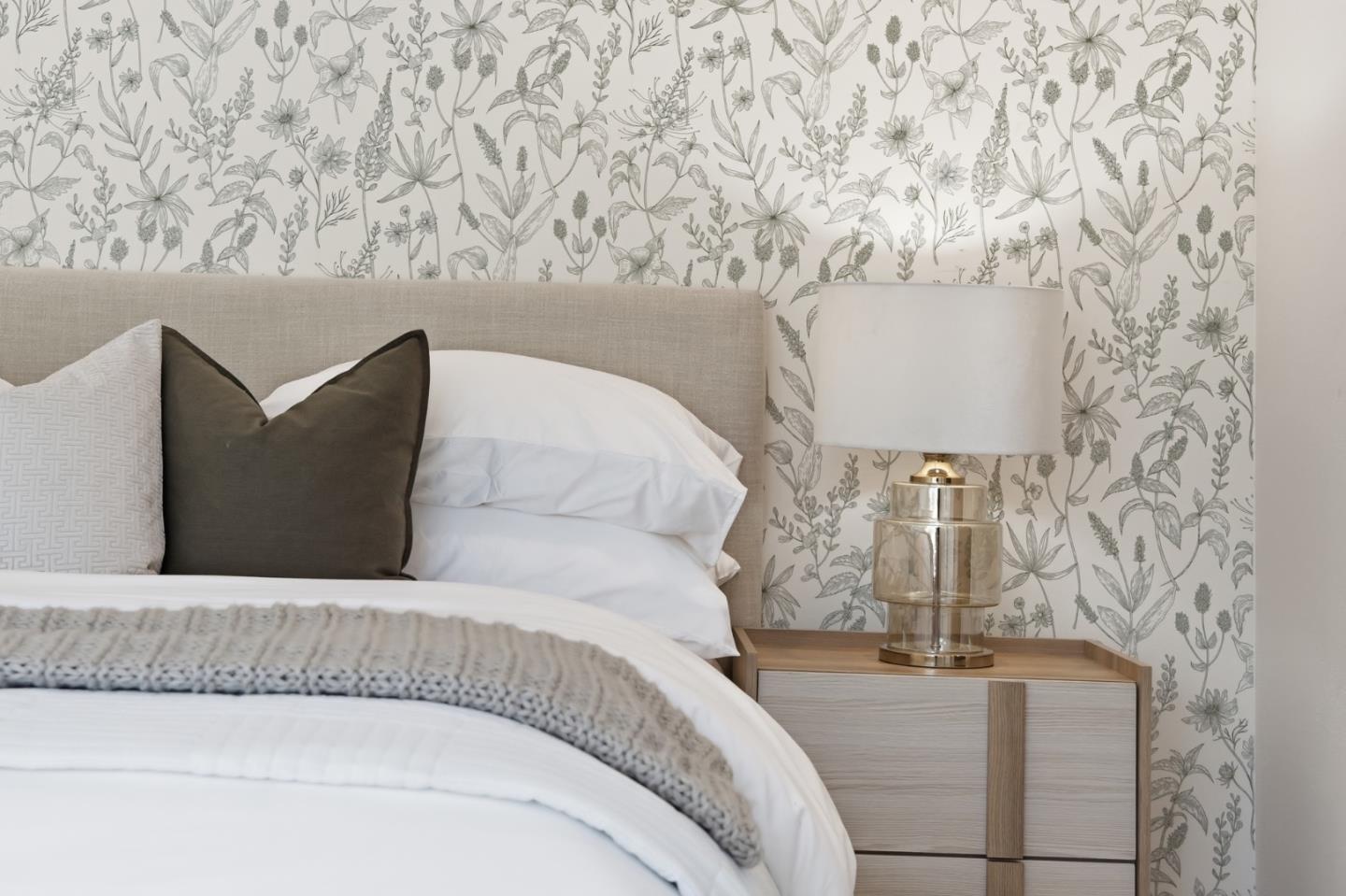 Bedroom with botanical wallpaper, a white bed, and a brass bedside lamp.