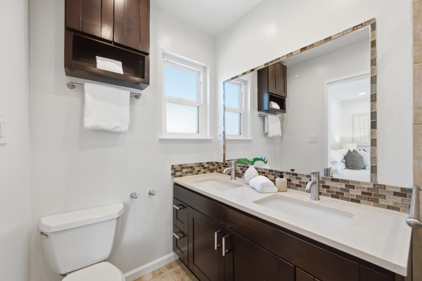 Bathroom with a dark wood double vanity, two sinks, a large mirror, and mosaic tile backsplash.