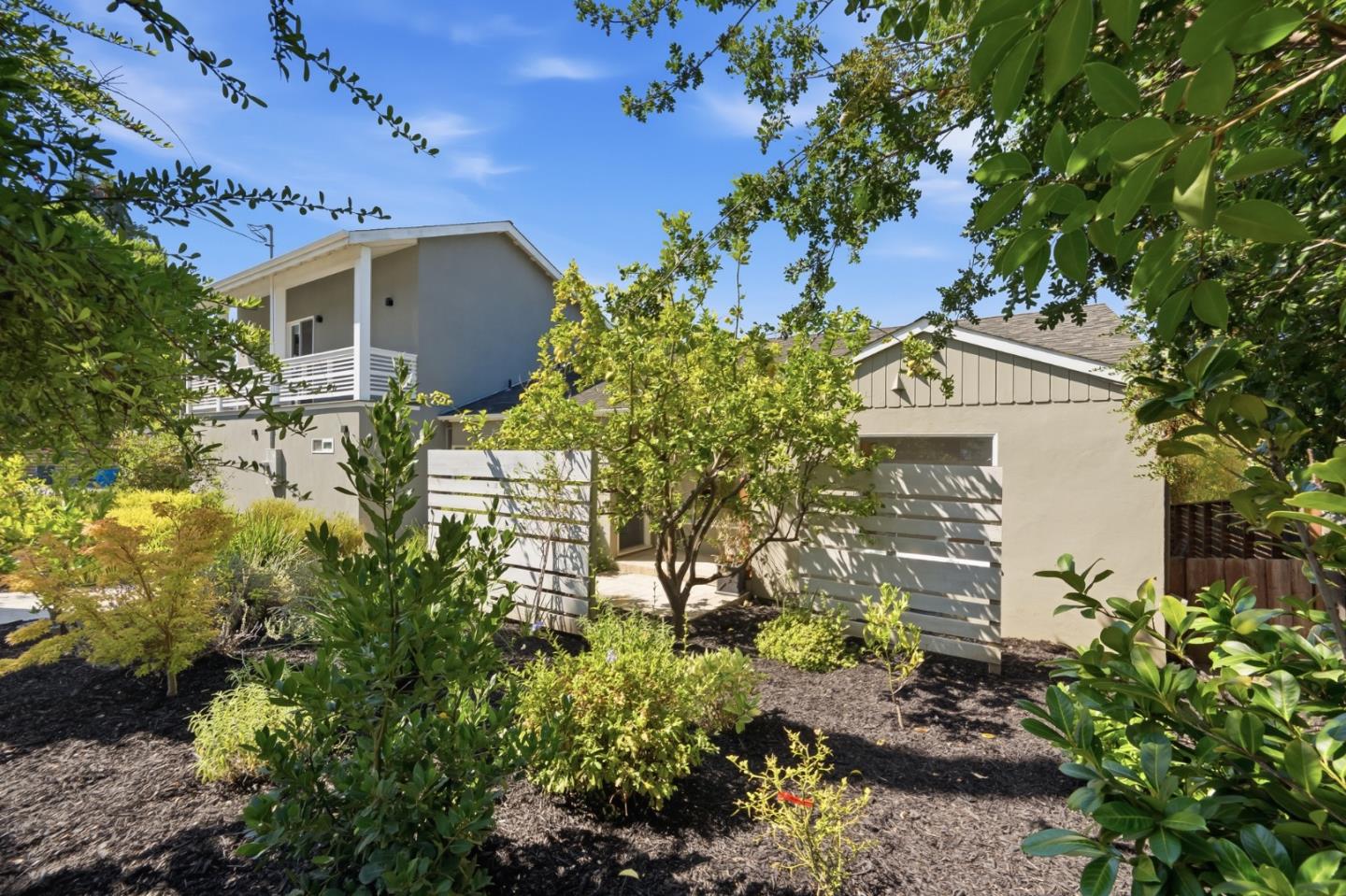 Gray two-story house behind a white slat fence and leafy landscaped garden.