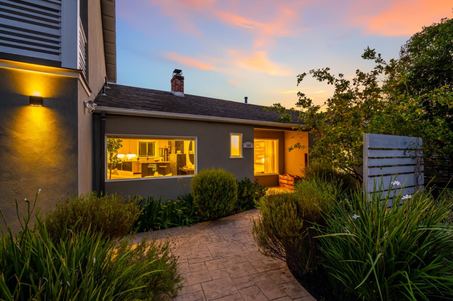 Home at dusk with a warmly lit entry, landscaped path, and colorful sunset sky.