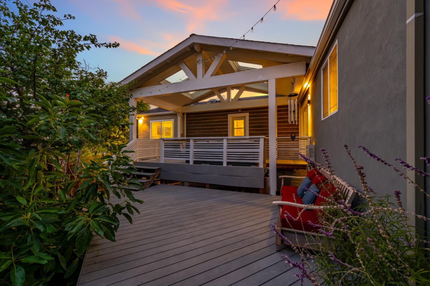 Covered wooden deck with white railings, string lights, and red cushioned seating at dusk.
