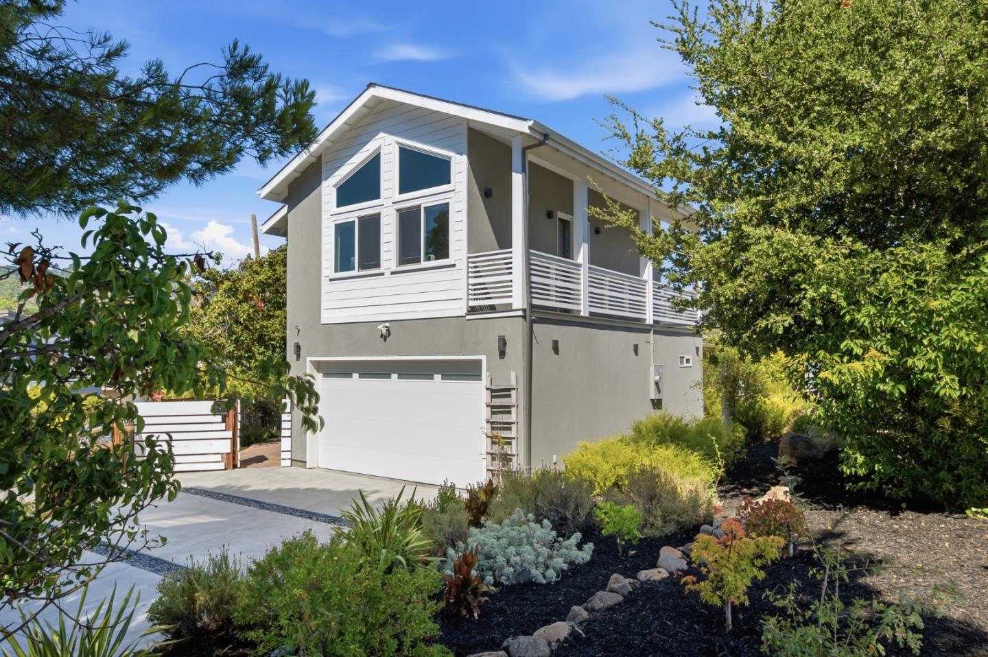 Modern two-story home with an upper balcony, attached garage, and landscaped front yard.
