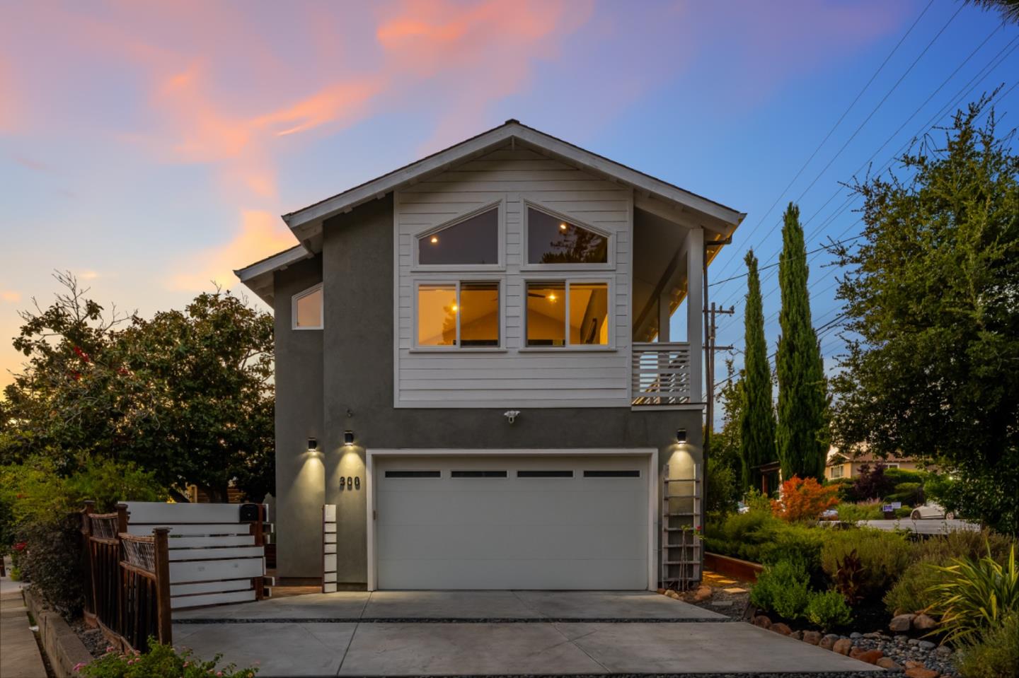 Modern two-story gray house with a large garage and lit windows at dusk.