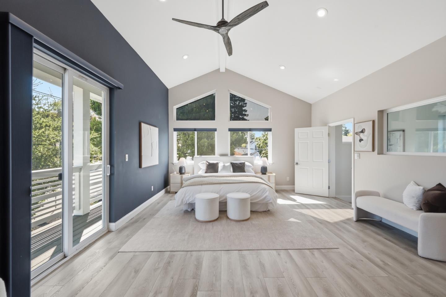 Bedroom with vaulted ceiling, blue accent wall, and sliding glass doors to a balcony.
