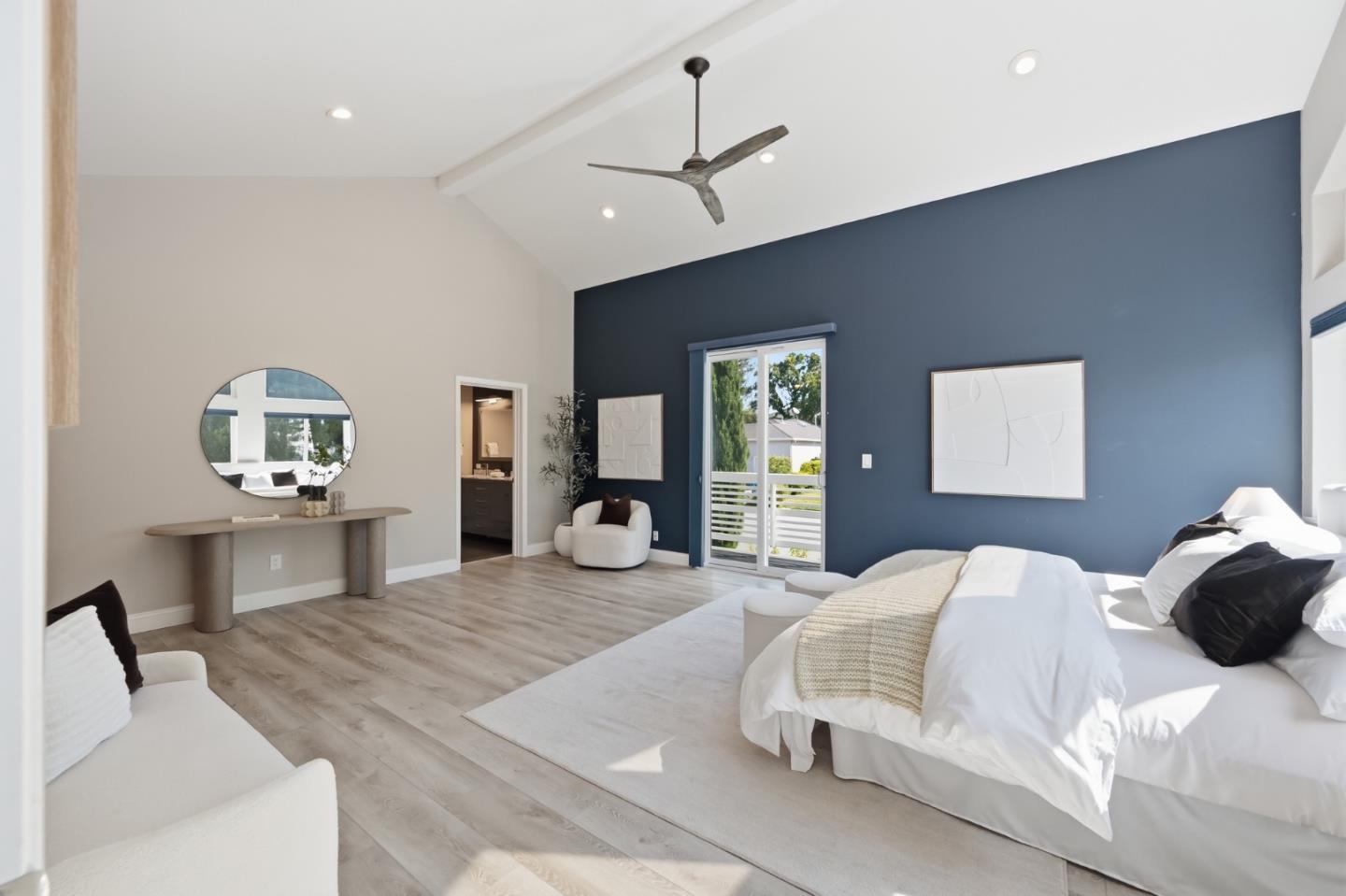 Staged bedroom with a vaulted ceiling, blue accent wall, and sliding glass doors to a balcony.
