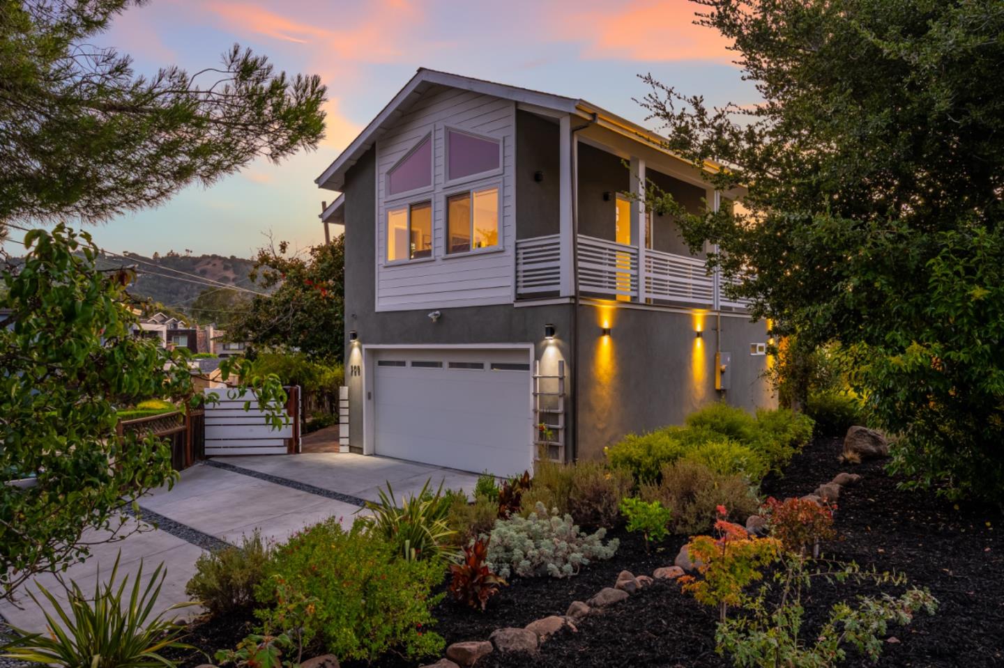Modern two-story home with a balcony and landscaped driveway glowing at dusk.