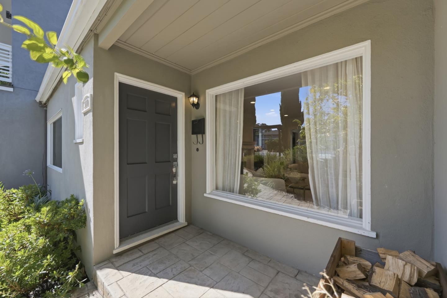 Home entrance with a dark front door, curtained window, tiled porch, and stacked firewood.