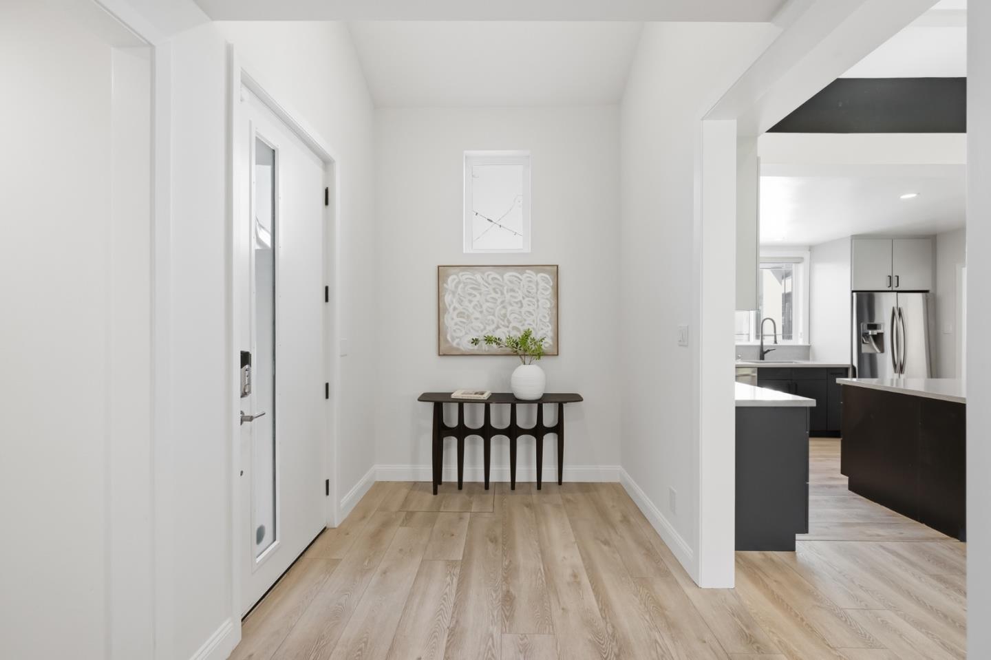 Entry foyer with a dark console table and wall art, opening to a modern kitchen.