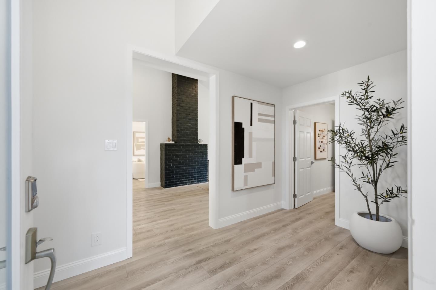 Modern entry hall with light wood floors and a black brick fireplace in the adjoining room.
