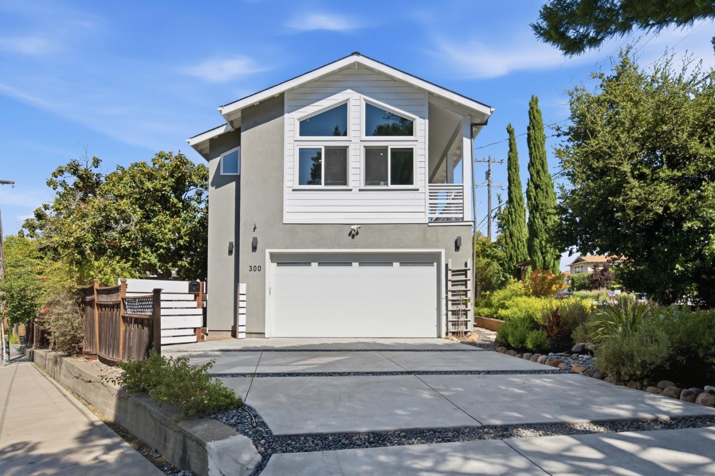 Two-story gray home with white garage, gable windows, wide driveway, and landscaped front yard.