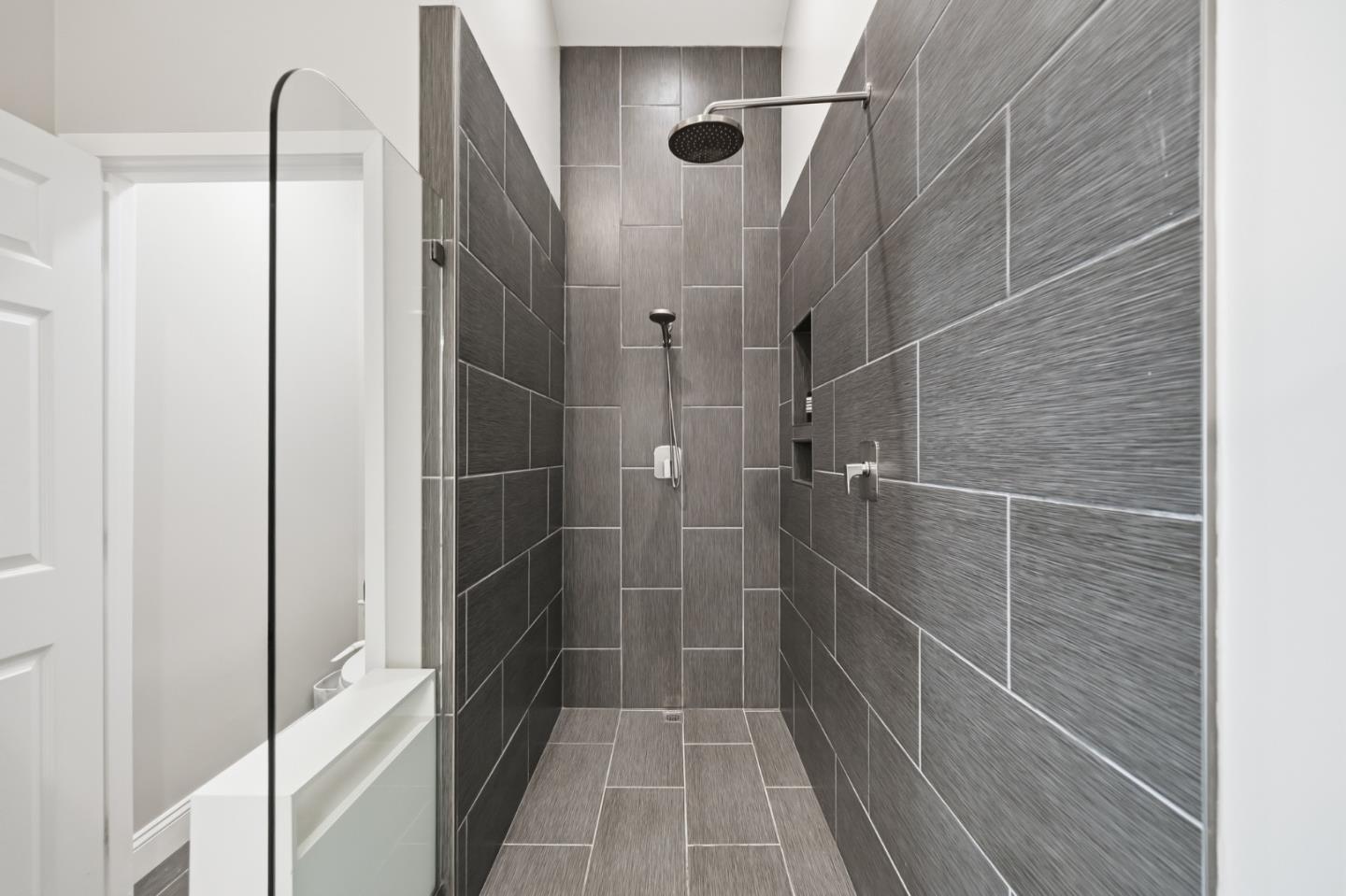 Walk-in shower with gray tile walls, a clear glass panel, and a rainfall showerhead.