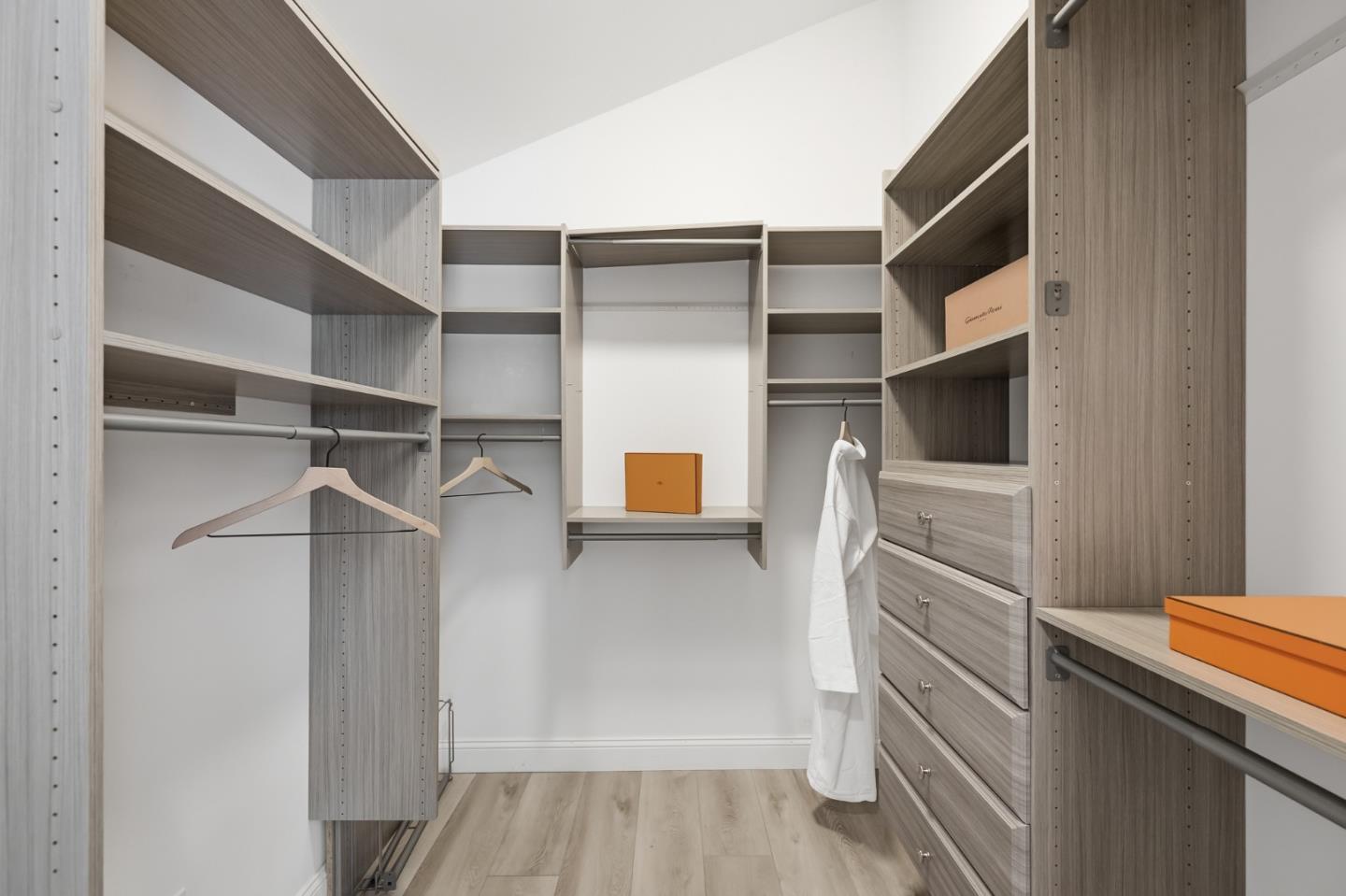 Walk-in closet with gray built-in shelving, drawers, hanging rods, and a white robe.