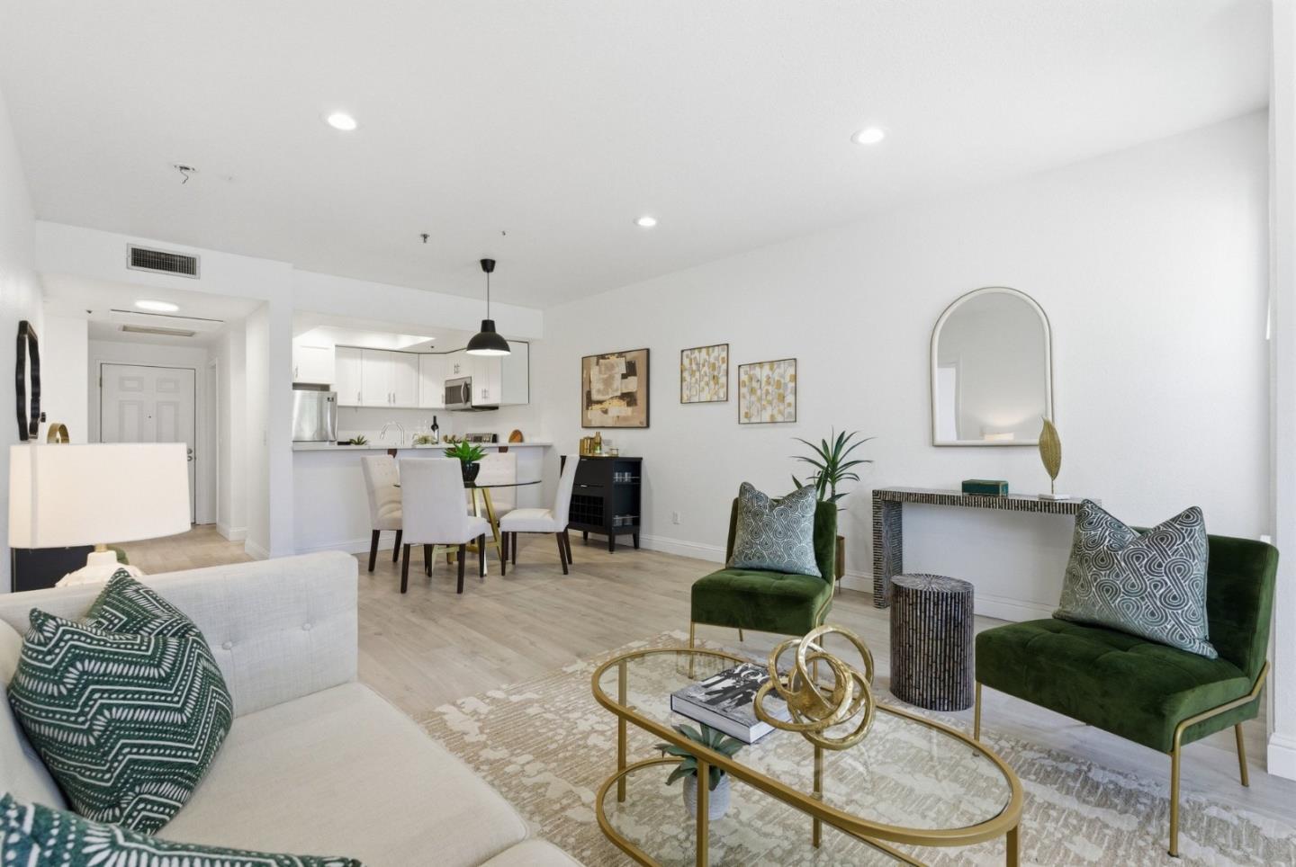 Open-plan living room with green accent chairs, a pale sofa, and kitchen dining area.