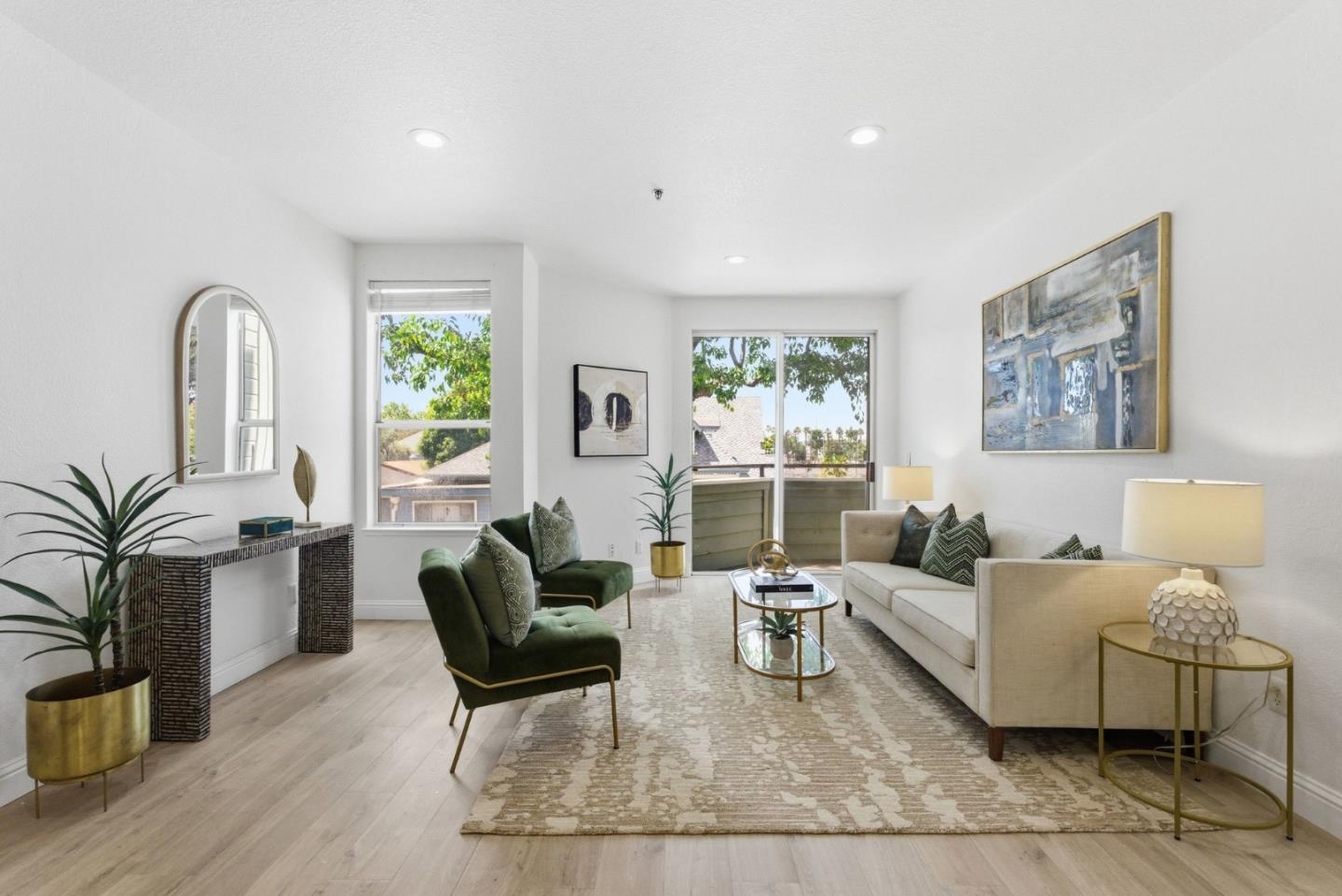 Staged living room with green armchairs, a white sofa, and large windows opening to a balcony.
