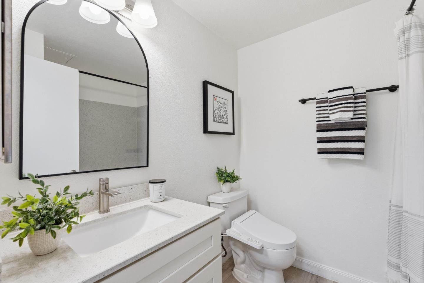 Bright bathroom with a white vanity, large black-framed mirror, and striped towels.