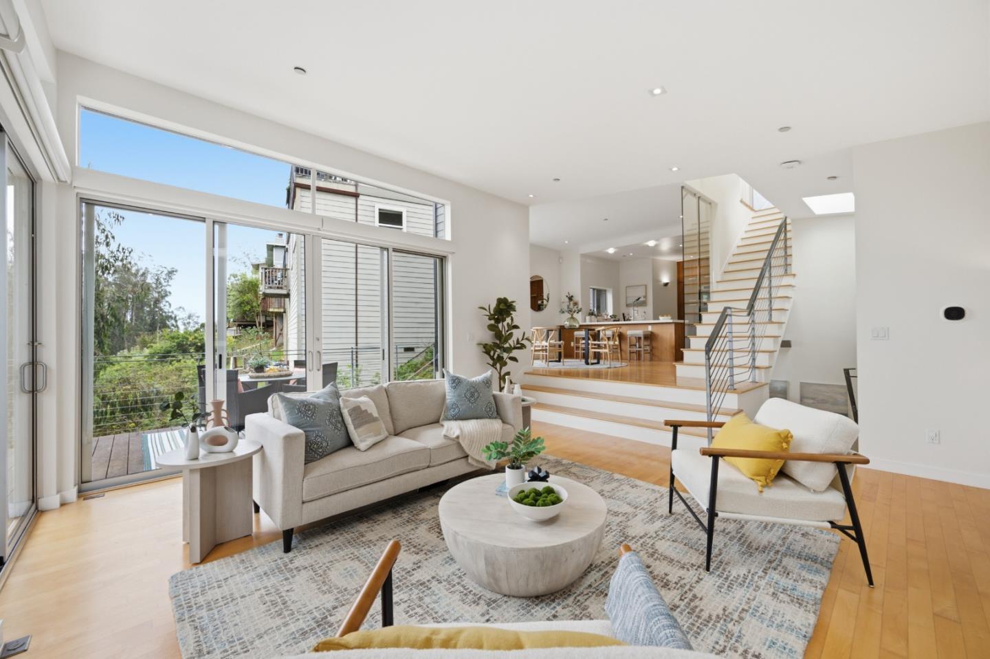 Open-plan living room with a beige sofa, sliding glass doors, and a staircase beside the kitchen.