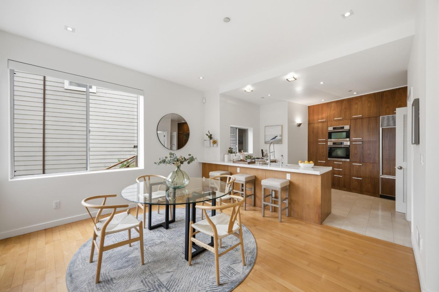 Dining area with a round glass table beside a wood-paneled kitchen island and built-in appliances.