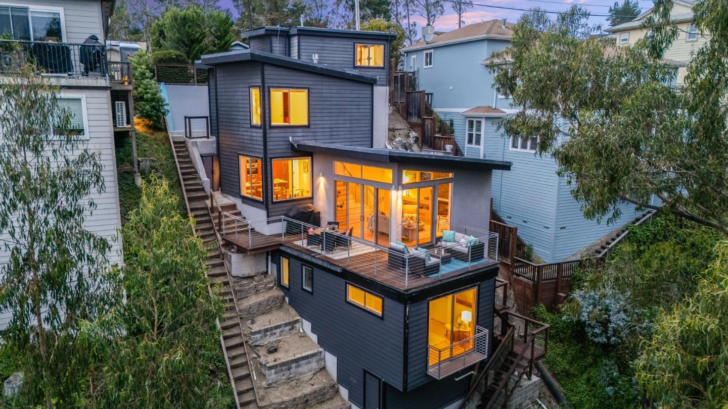Modern hillside home with a broad deck, cable railings, and warmly lit windows at dusk.