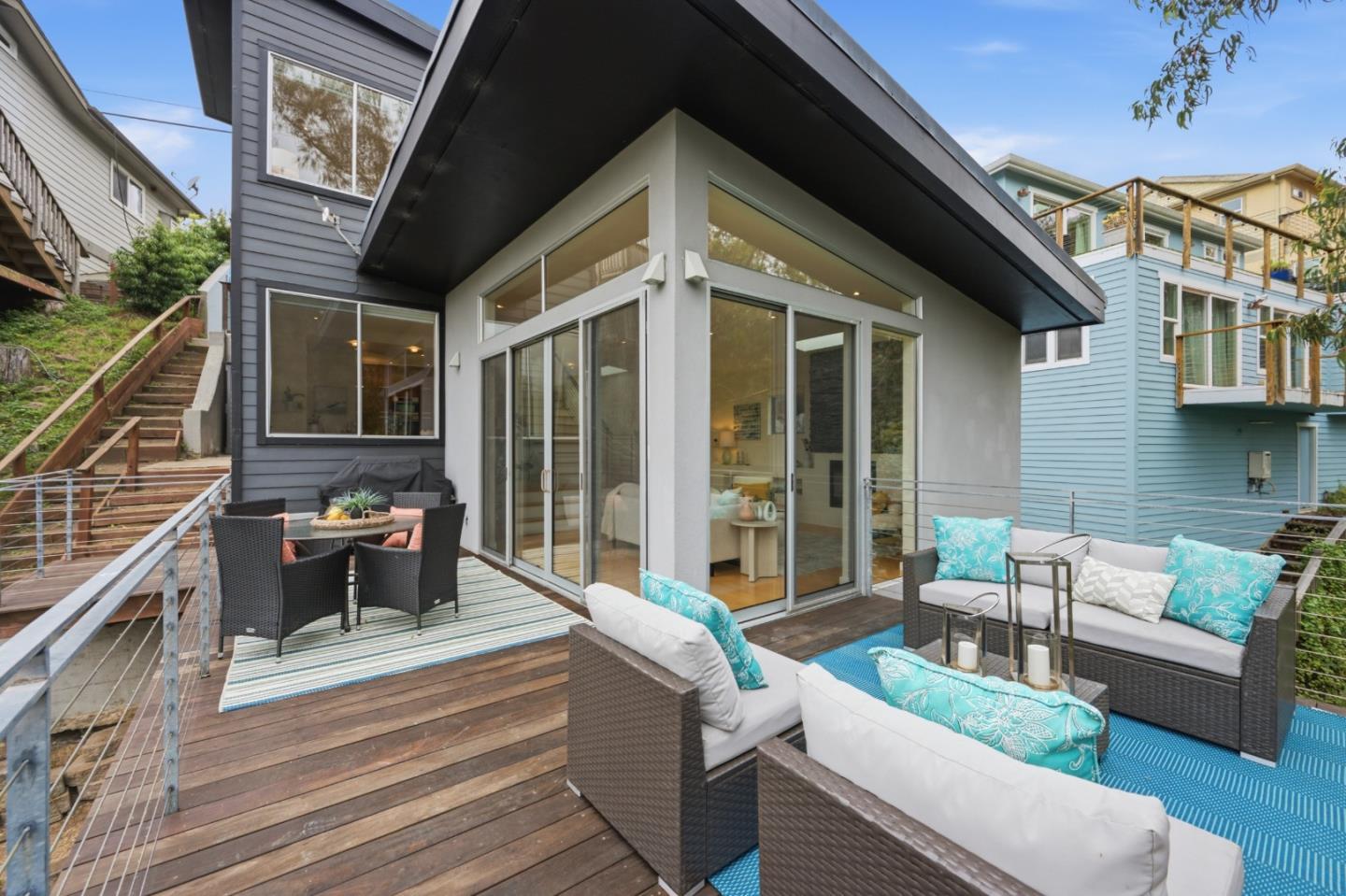 Modern home with a furnished wooden deck, sliding glass doors, and turquoise-accented outdoor lounge seating.