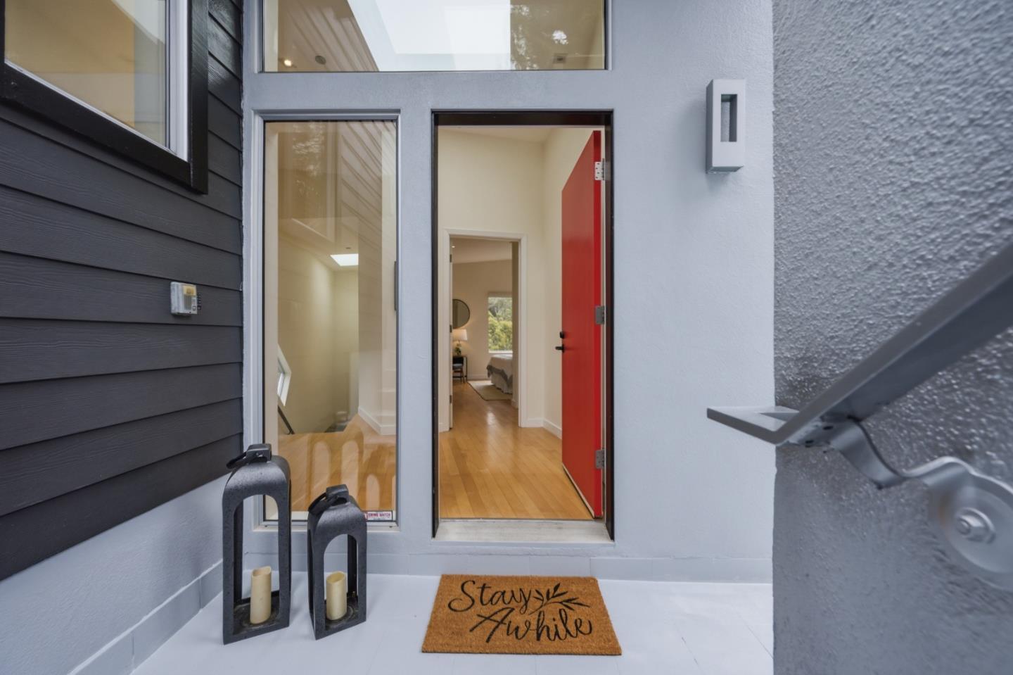 Home entrance with an open red door, glass sidelights, and lanterns beside a welcome mat.