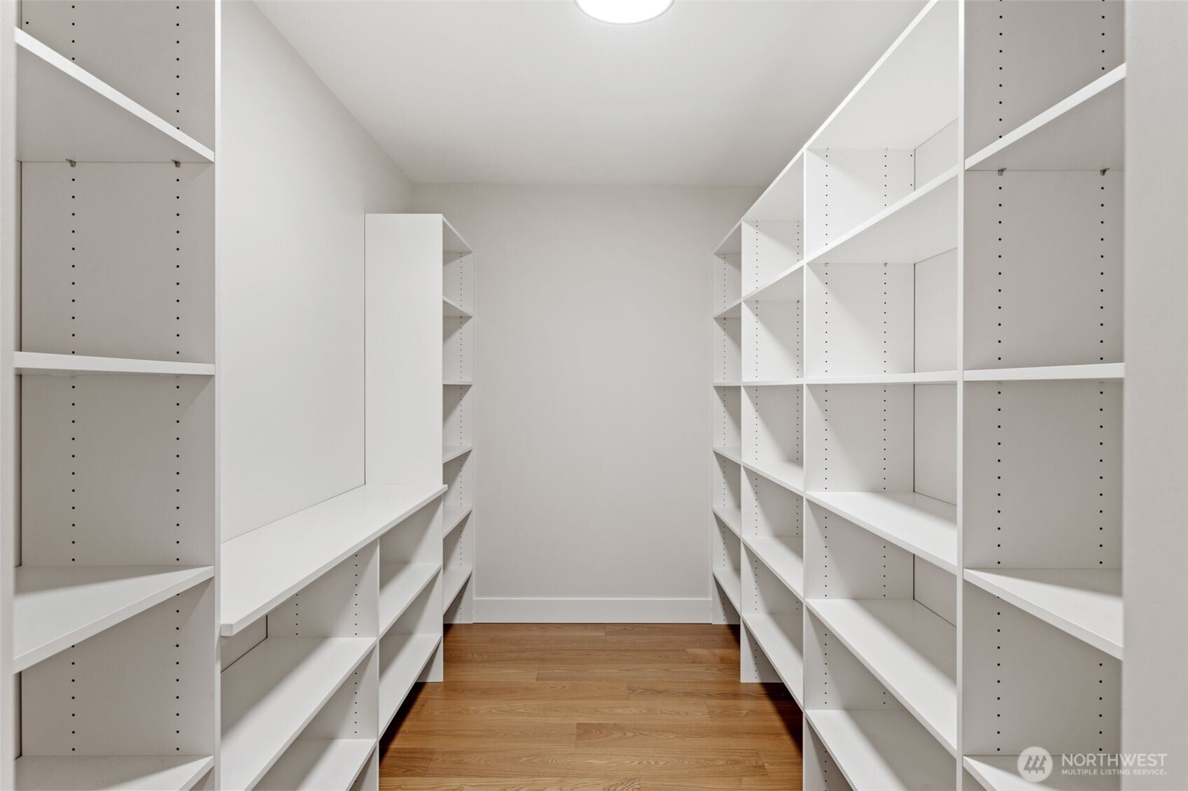 Walk-in storage room with floor-to-ceiling white shelving and wood flooring.