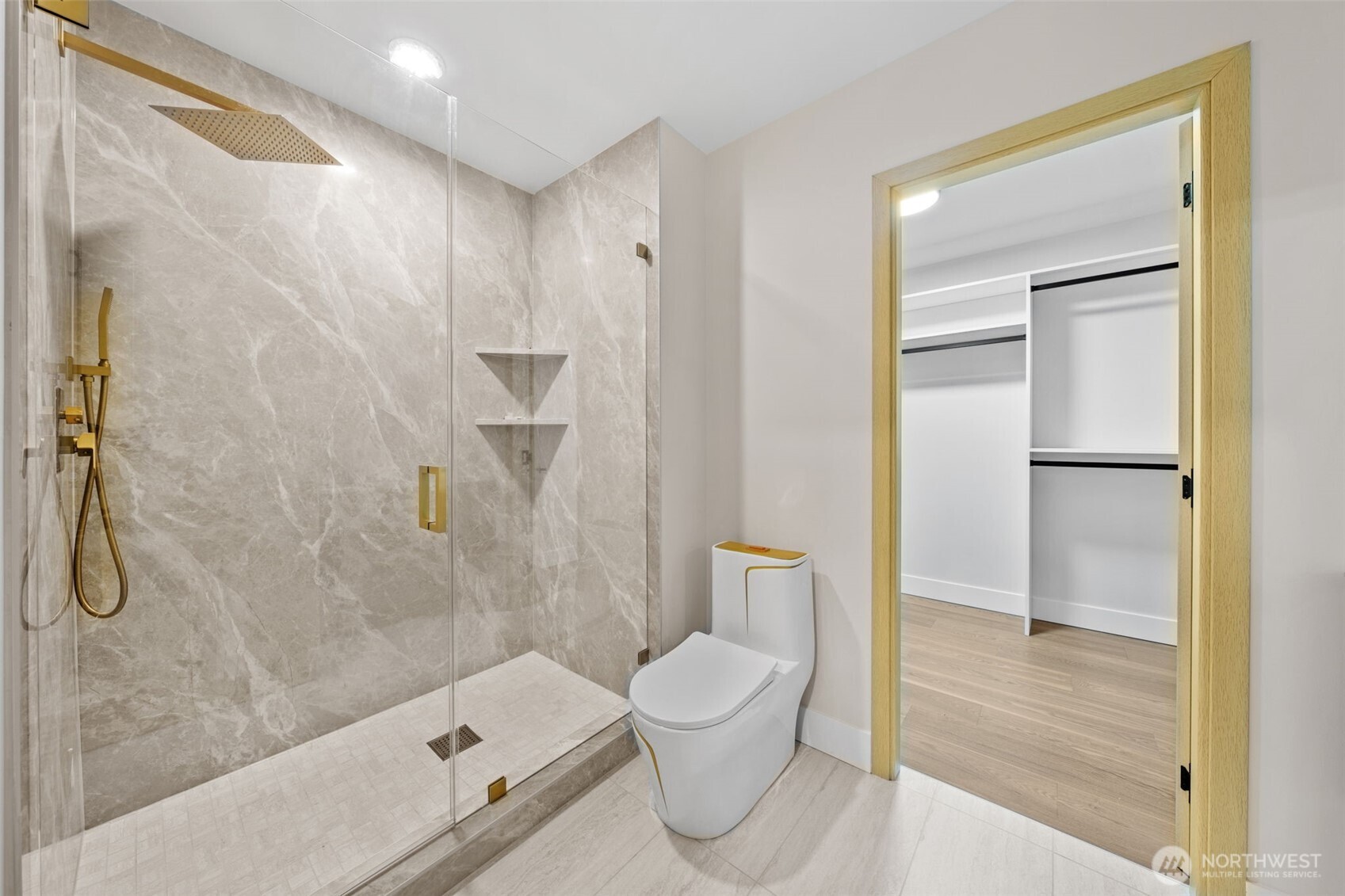 Bathroom with a glass-enclosed marble shower, gold fixtures, and a doorway to a walk-in closet.