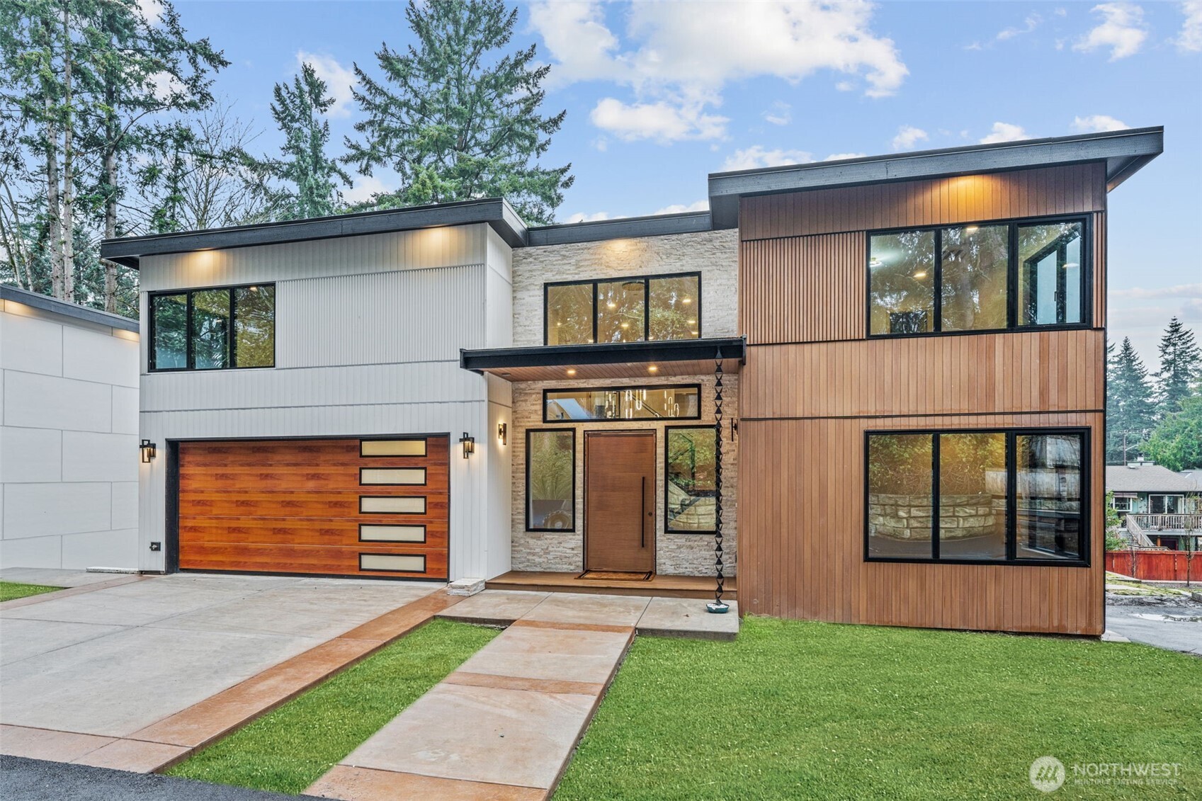 Modern two-story home with mixed wood and light siding, stone accents, and a wide wood garage door.