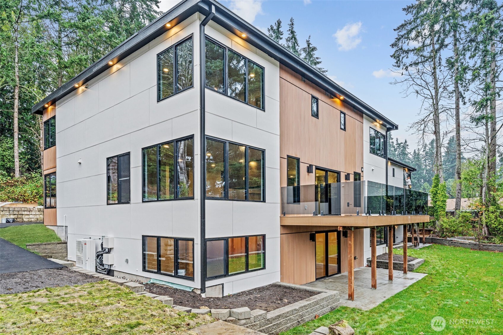 Modern two-story house with white and wood siding, large windows, and a raised glass-railed deck.