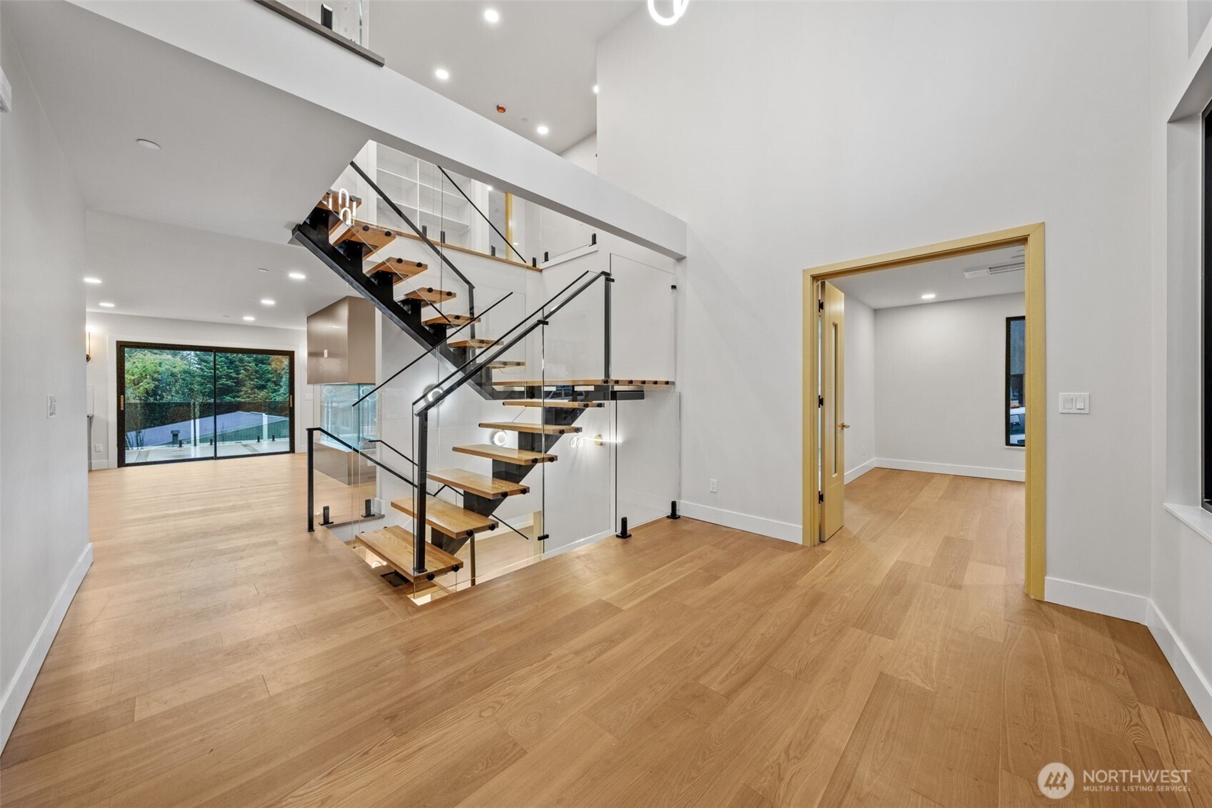 Entry foyer with a glass-and-wood staircase, light oak floors, and sliding doors to the patio.