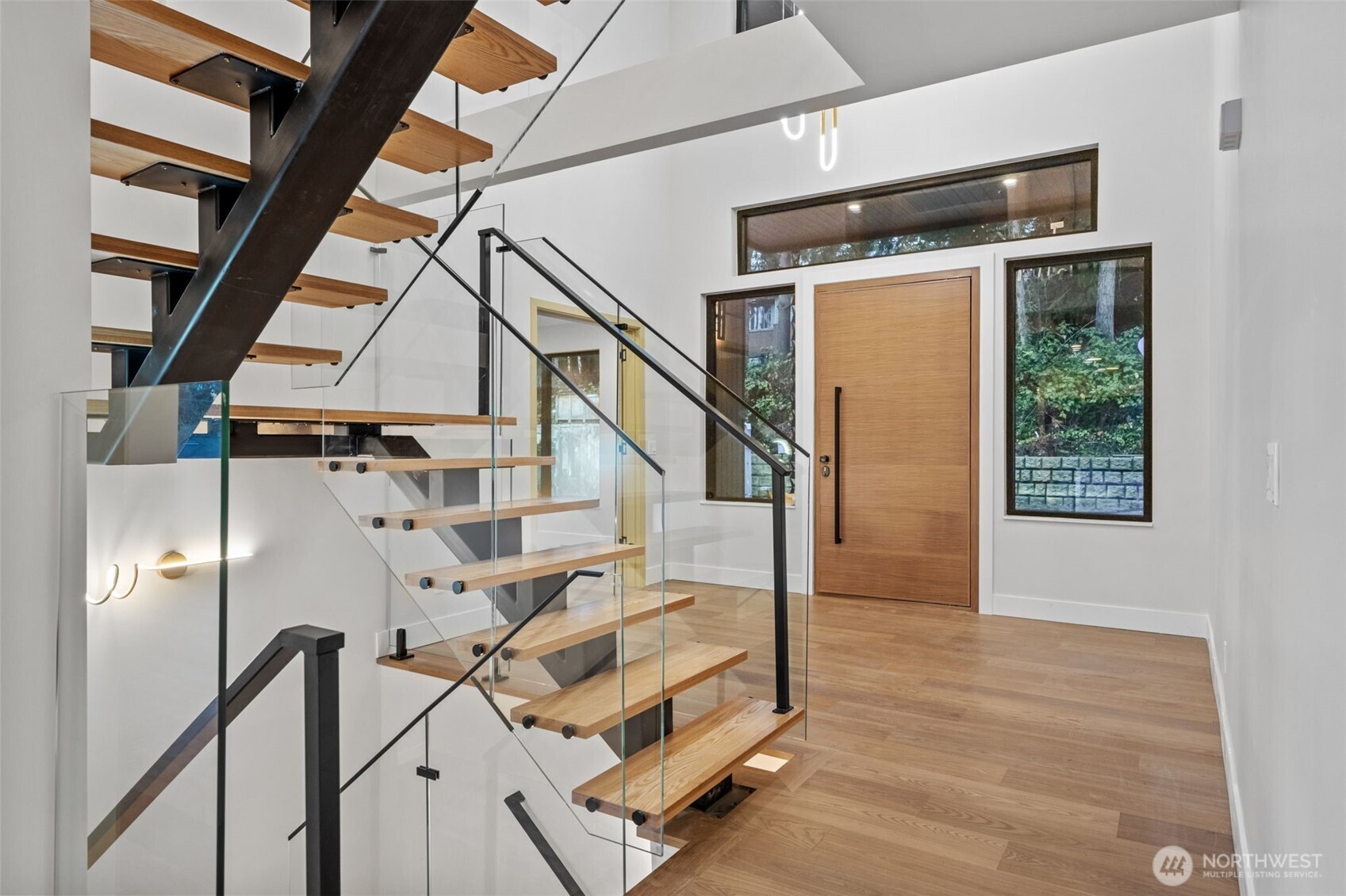 Entry foyer with a floating wood staircase, glass railings, and a tall wooden front door.