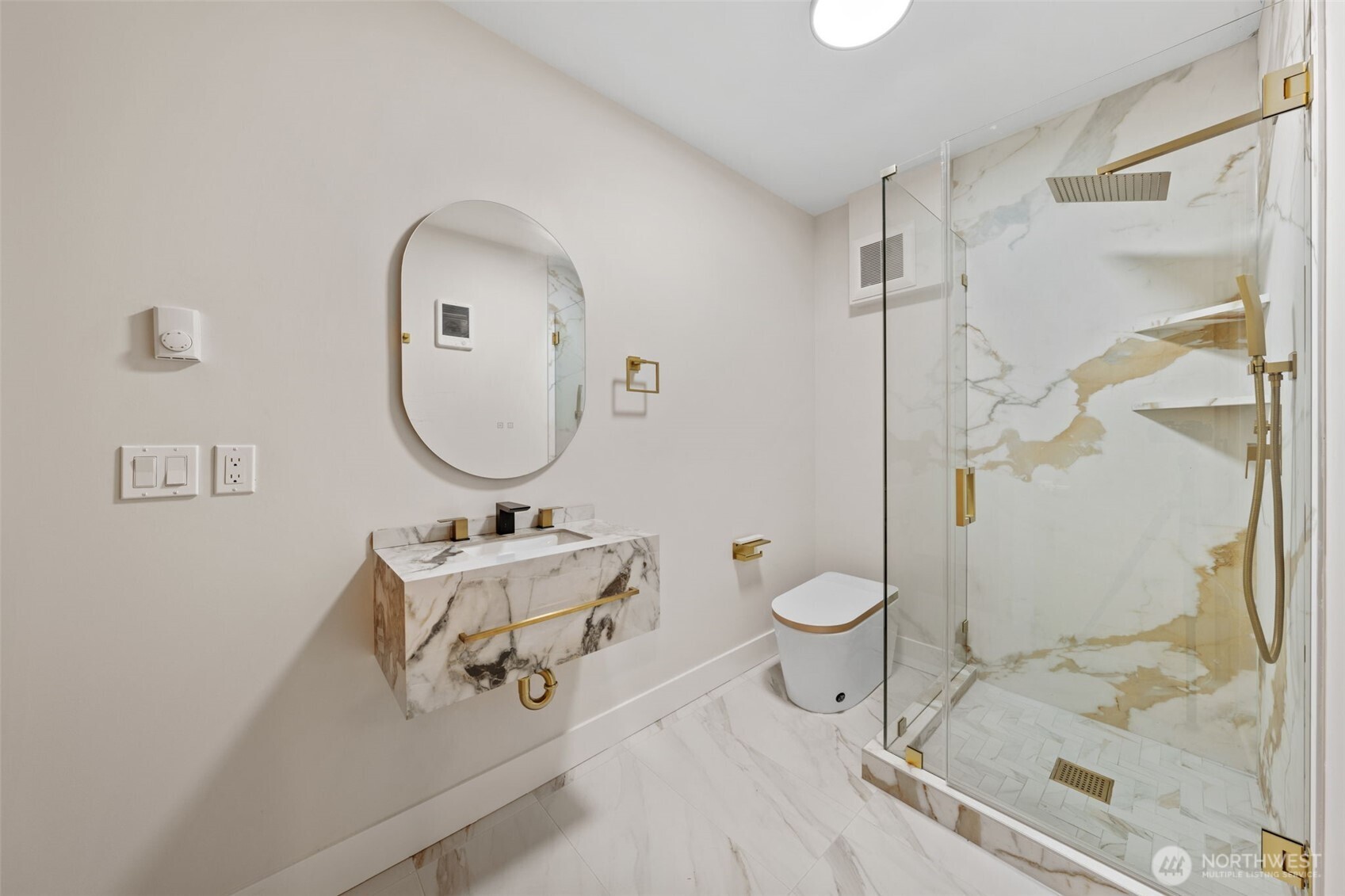 Bathroom with a floating marble vanity and glass-enclosed shower with gold fixtures.