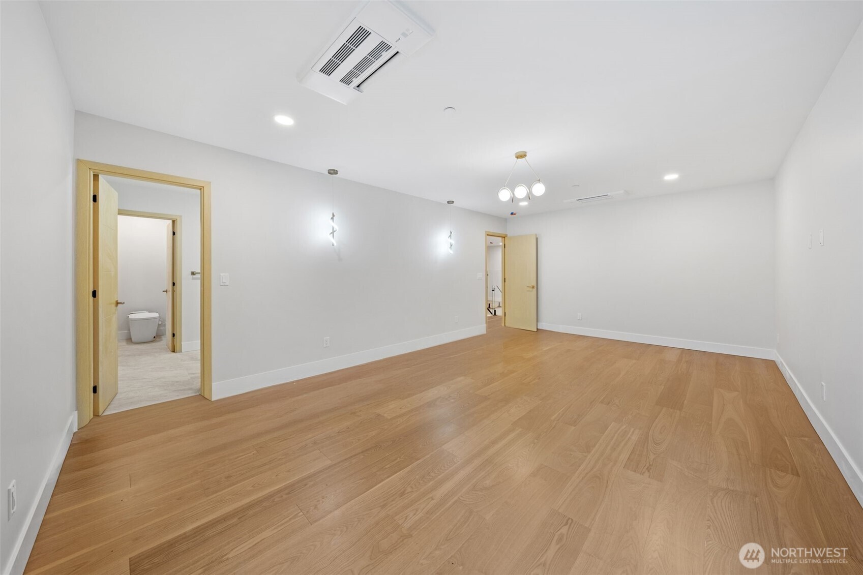 Empty room with light wood flooring, recessed lighting, and an open bathroom doorway.