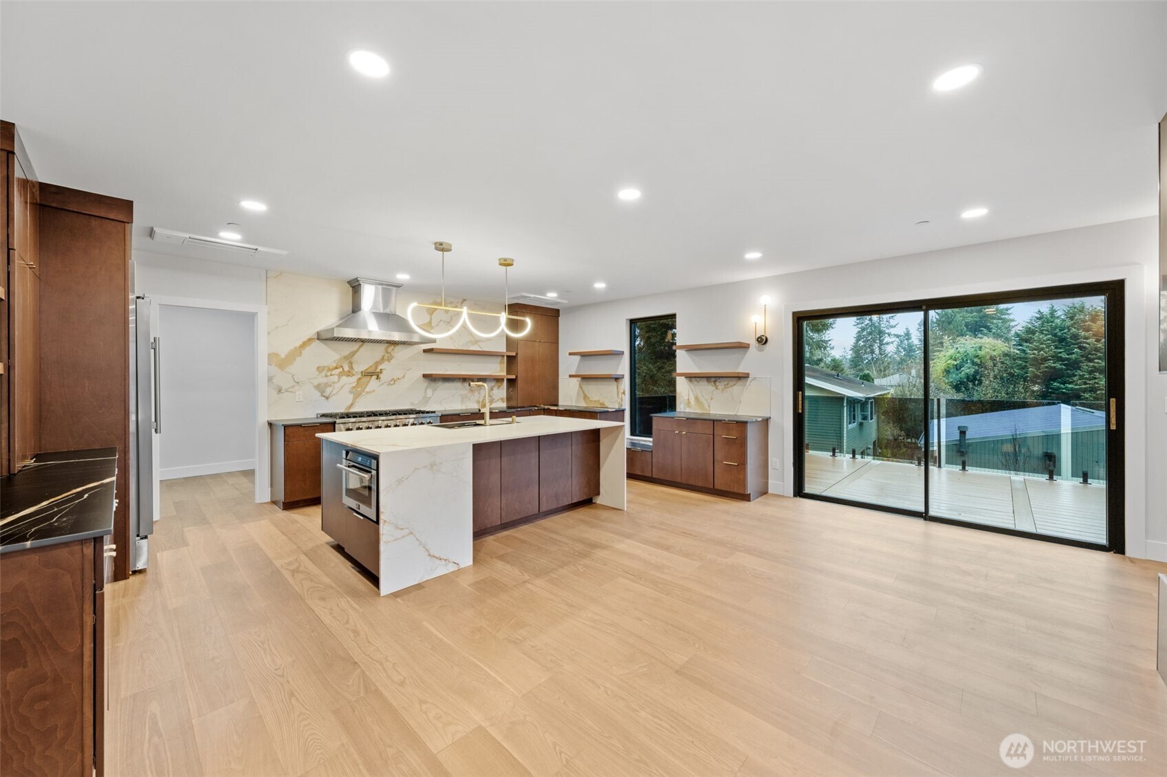 Modern kitchen with a marble-veined island, walnut cabinetry, and sliding doors to a deck.