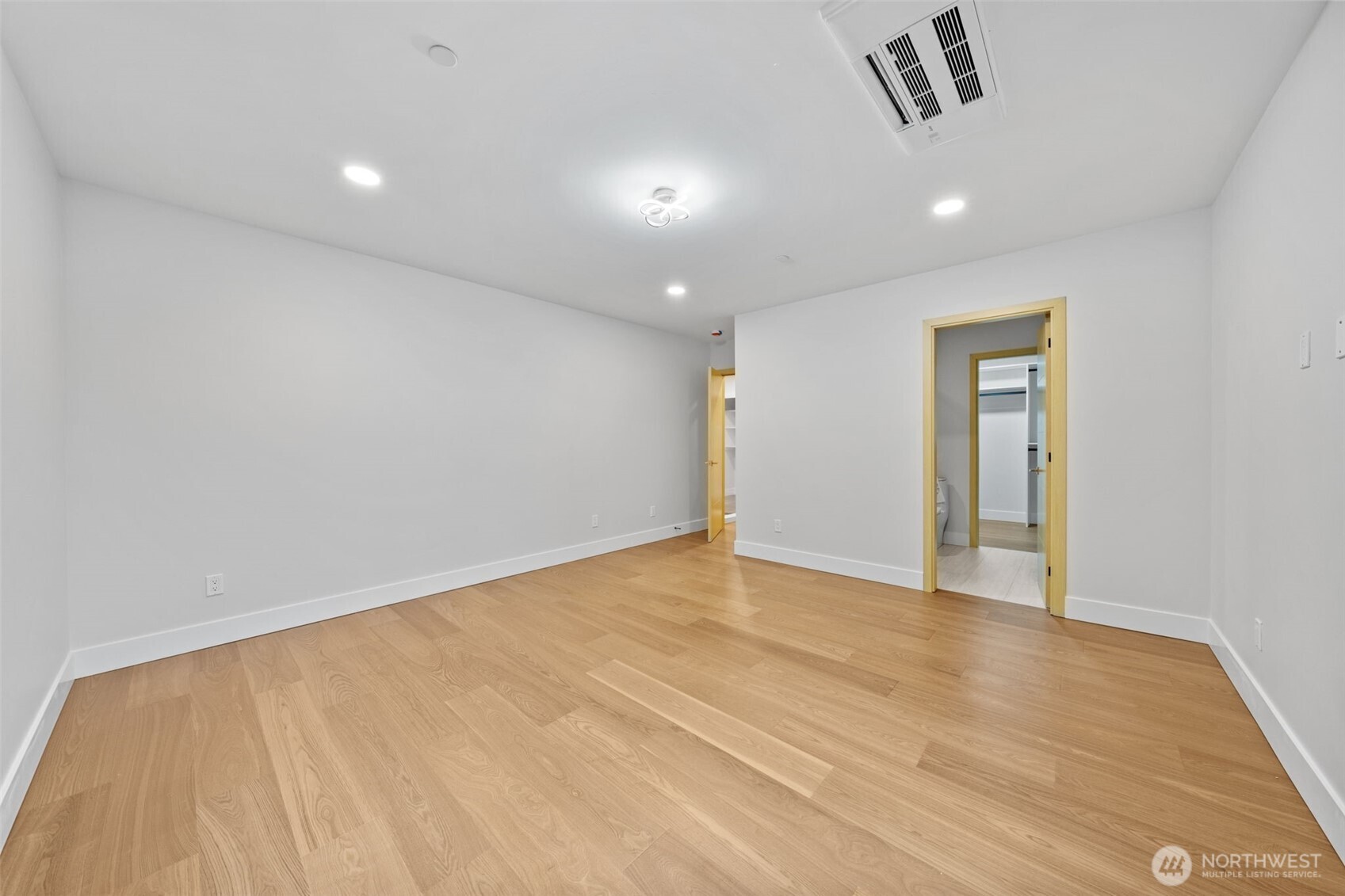 Empty room with light wood flooring, recessed lights, and doorways to a bathroom and closet.