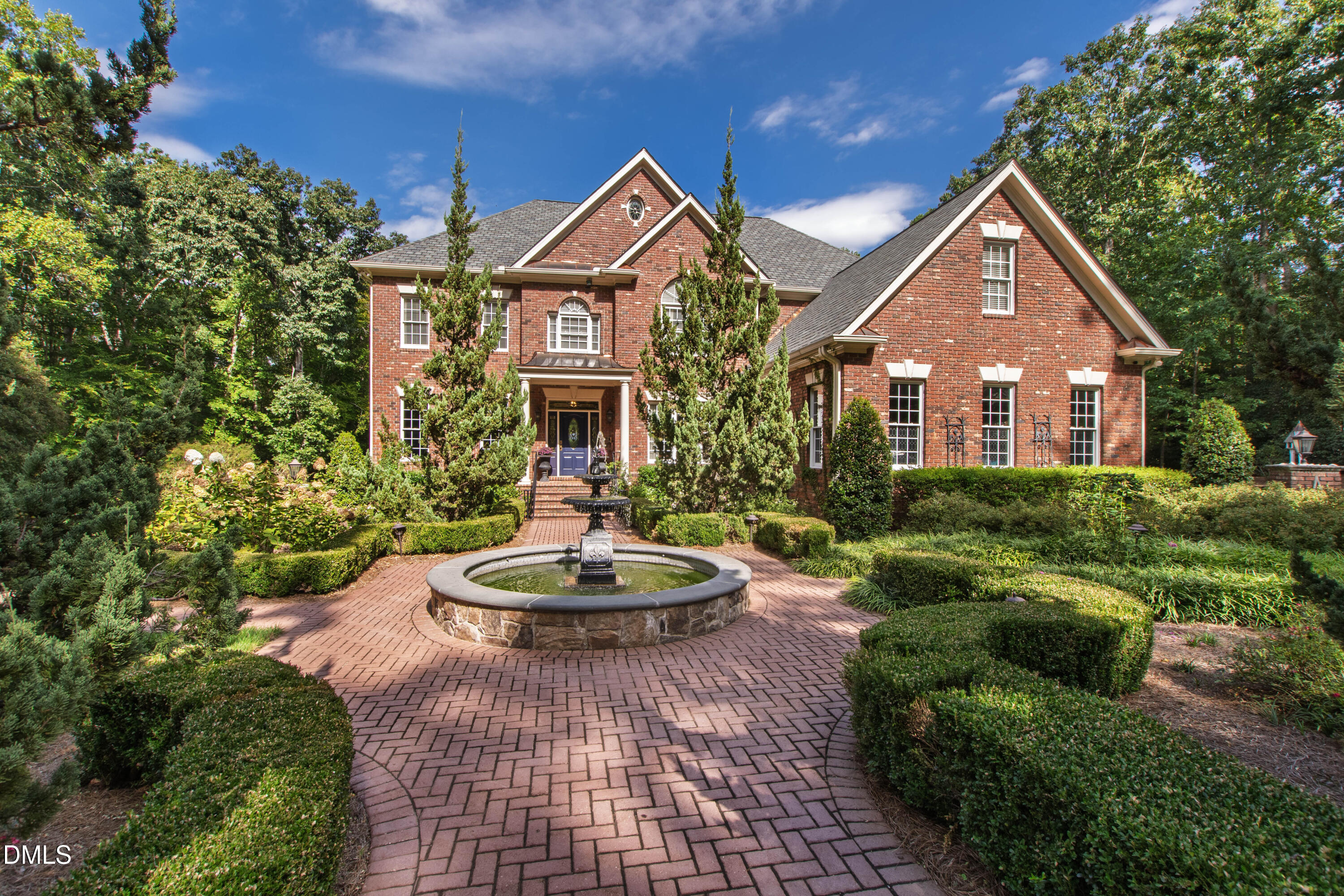 Red brick house with a circular fountain and landscaped brick walkway.