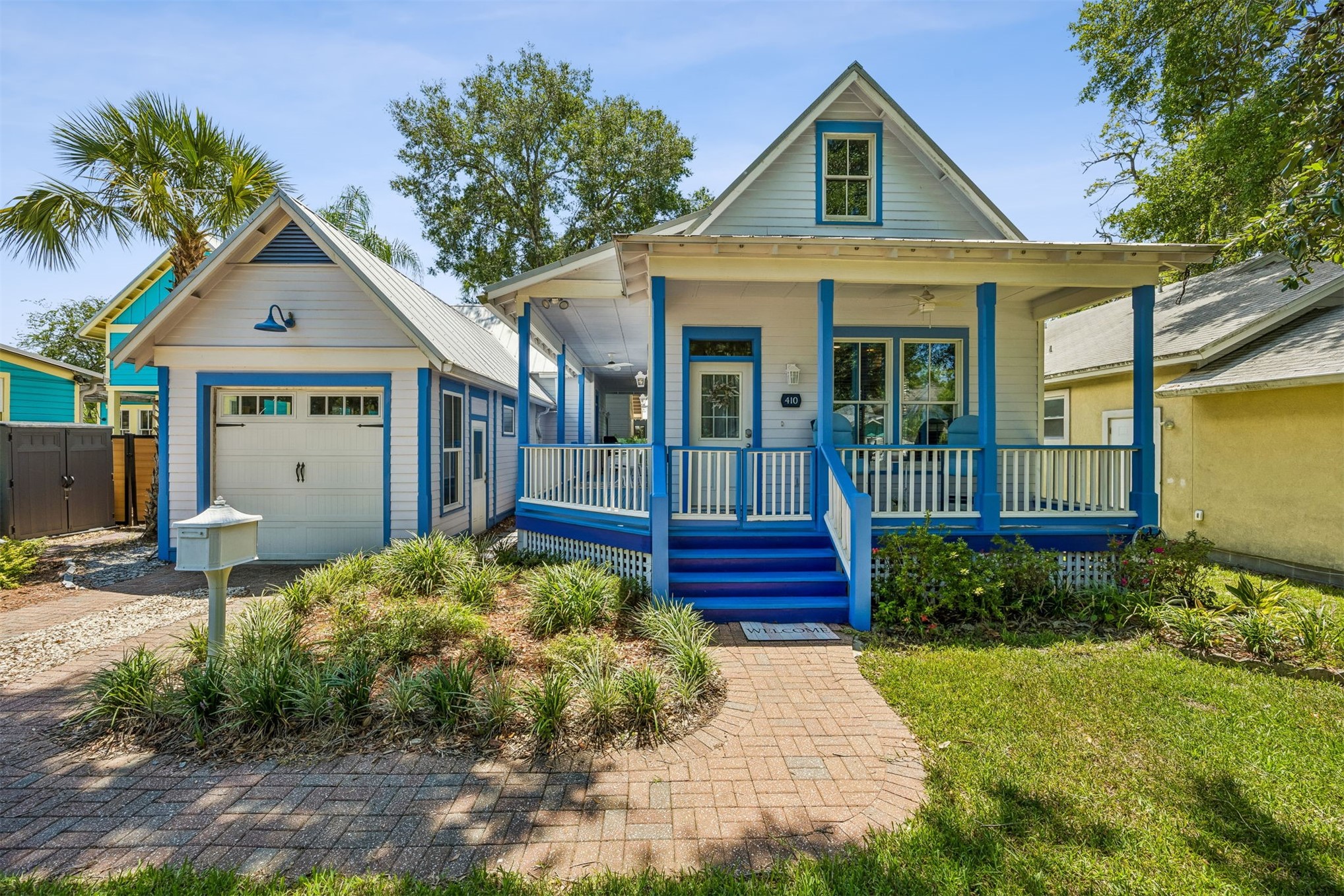 Gabled house with blue trim, a covered porch, attached garage, and landscaped brick walkway.