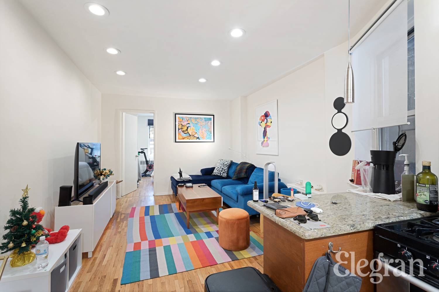 Open-plan living room and kitchen with a blue sectional, colorful striped rug, and stone island.