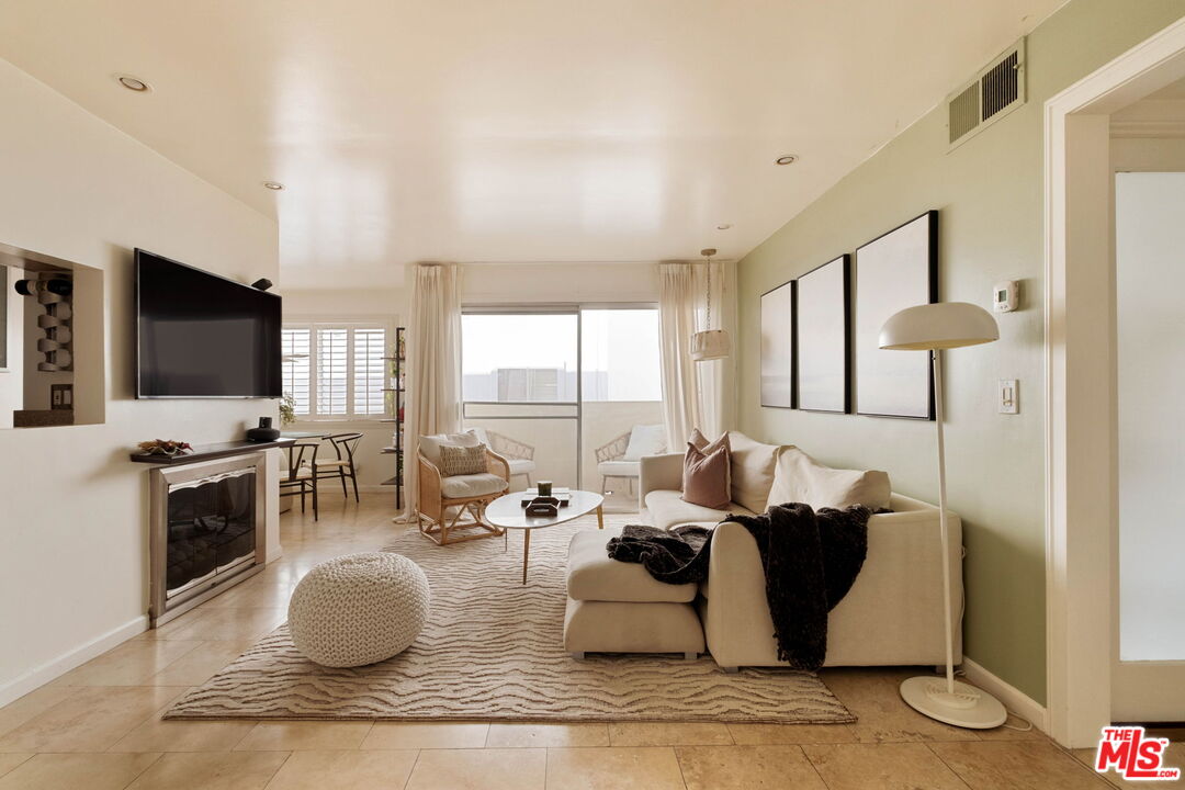 Furnished living room with a cream sectional, fireplace, and large curtained windows.