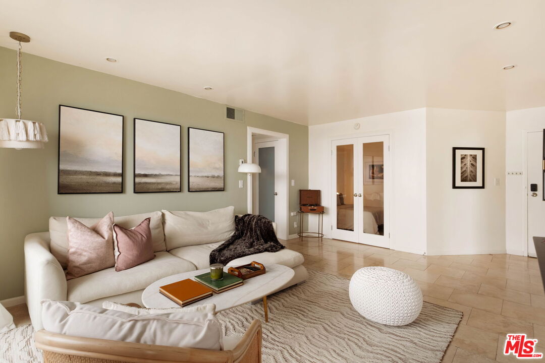 Staged living room with a cream sectional, sage-green accent wall, and glass-paneled double doors.