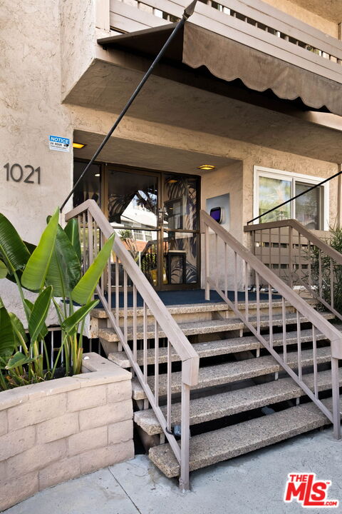 Residential building entrance marked 1021, with concrete steps, metal railings, and tropical plants.