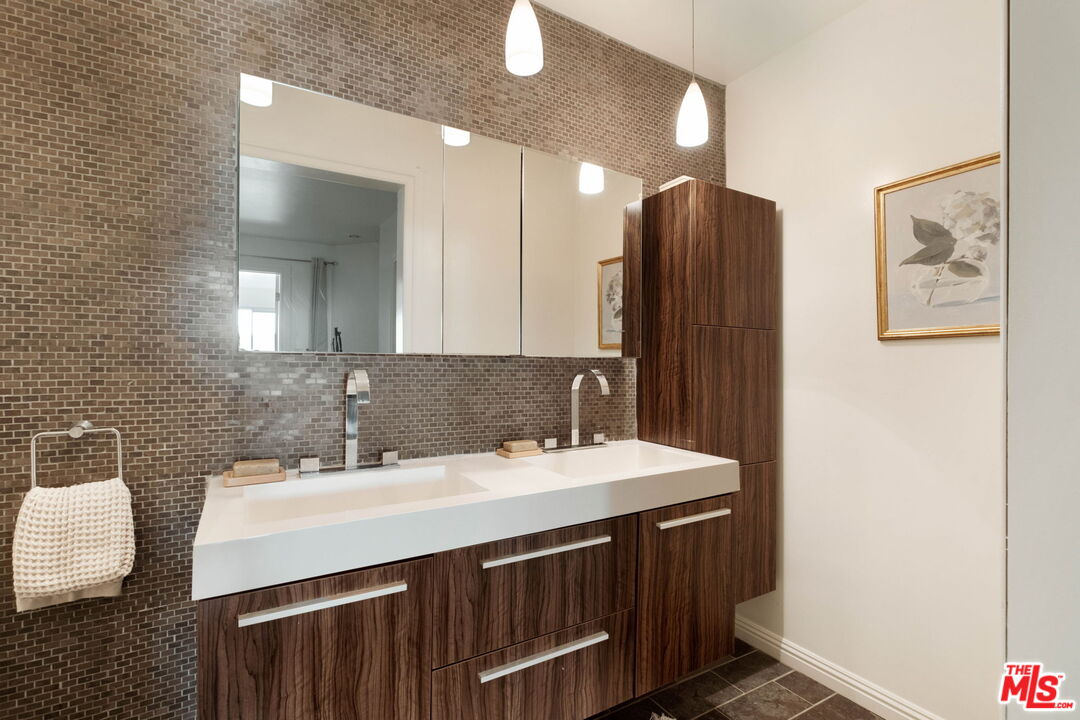 Bathroom with a double-sink vanity, dark wood cabinetry, tiled backsplash, and pendant lights.